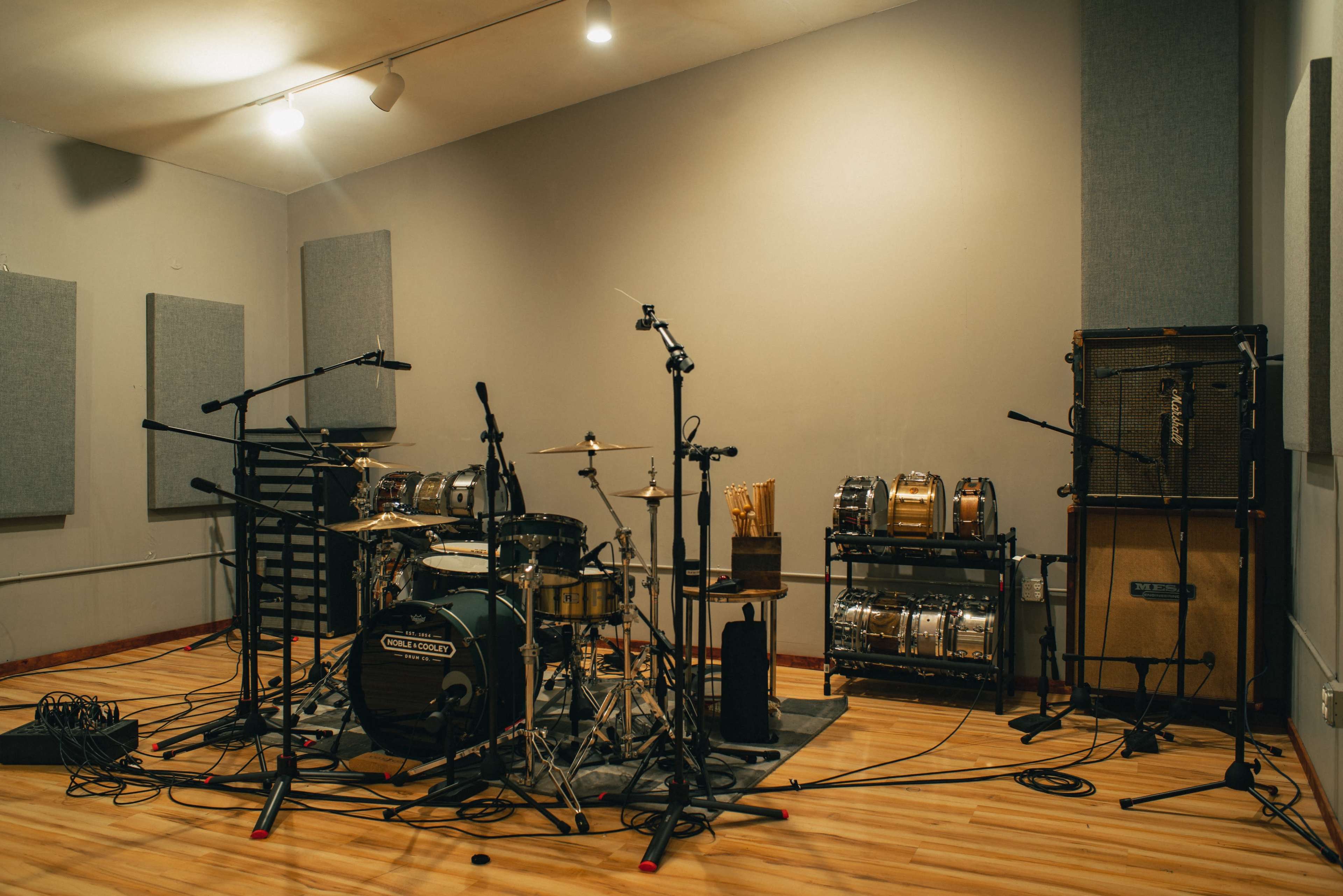 A music recording studio featuring a drum set surrounded by microphones, amplifiers, and various percussion instruments.