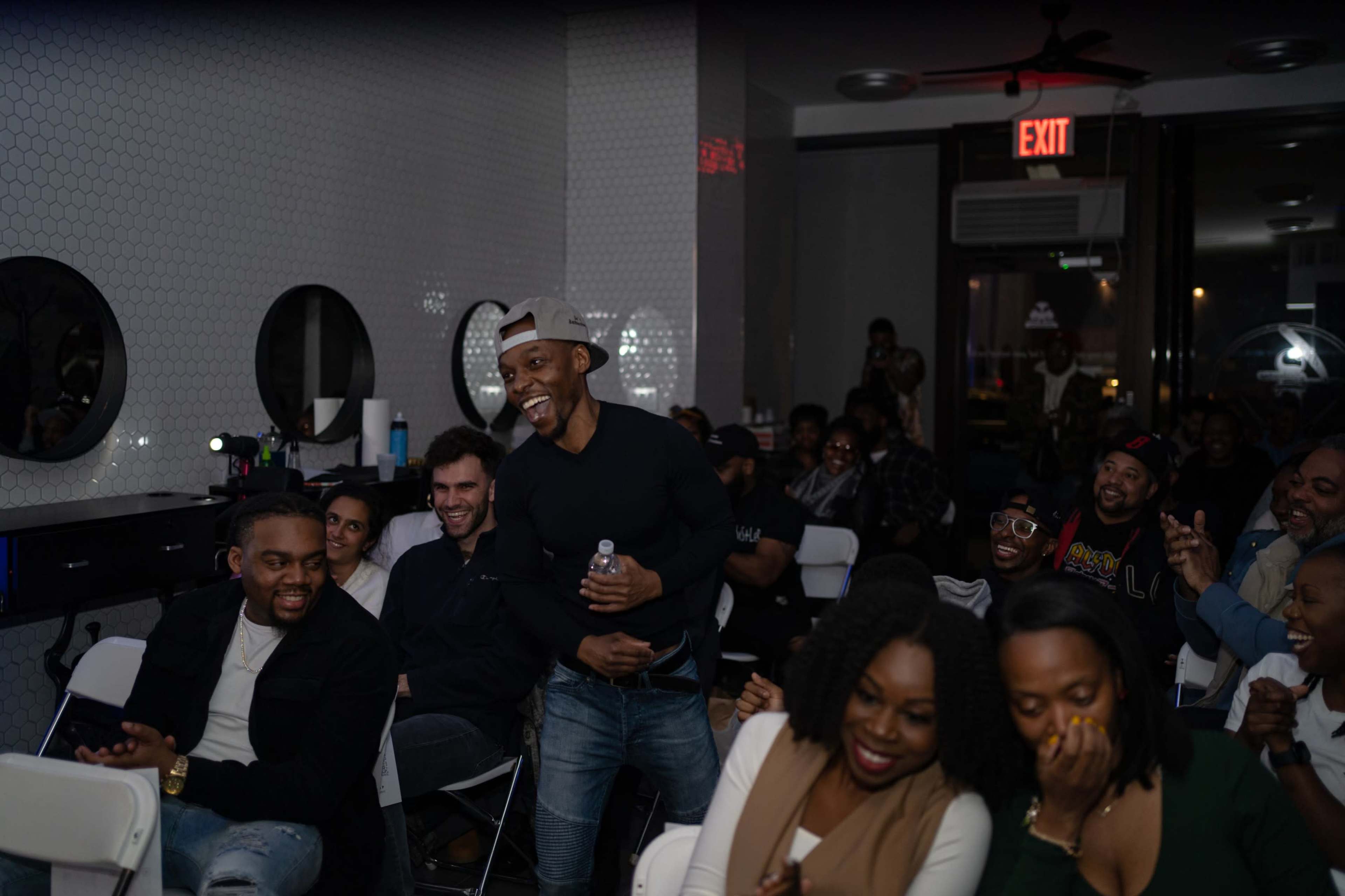 A diverse group of people is seated in a modern venue, engaging with a speaker and laughing together during an event.