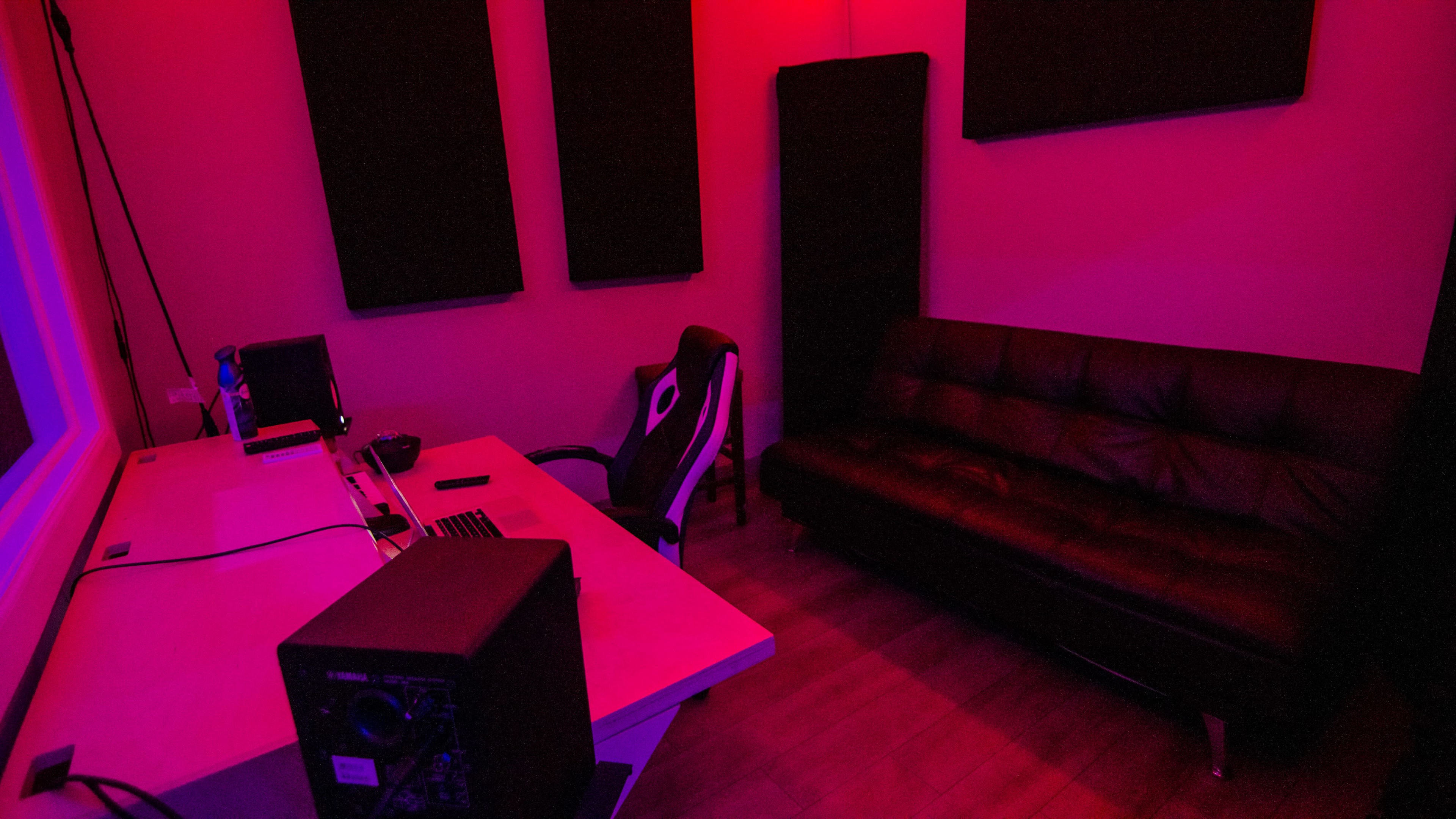A dimly lit room with a black couch, a desk with computer equipment, and soundproofing panels on the walls.