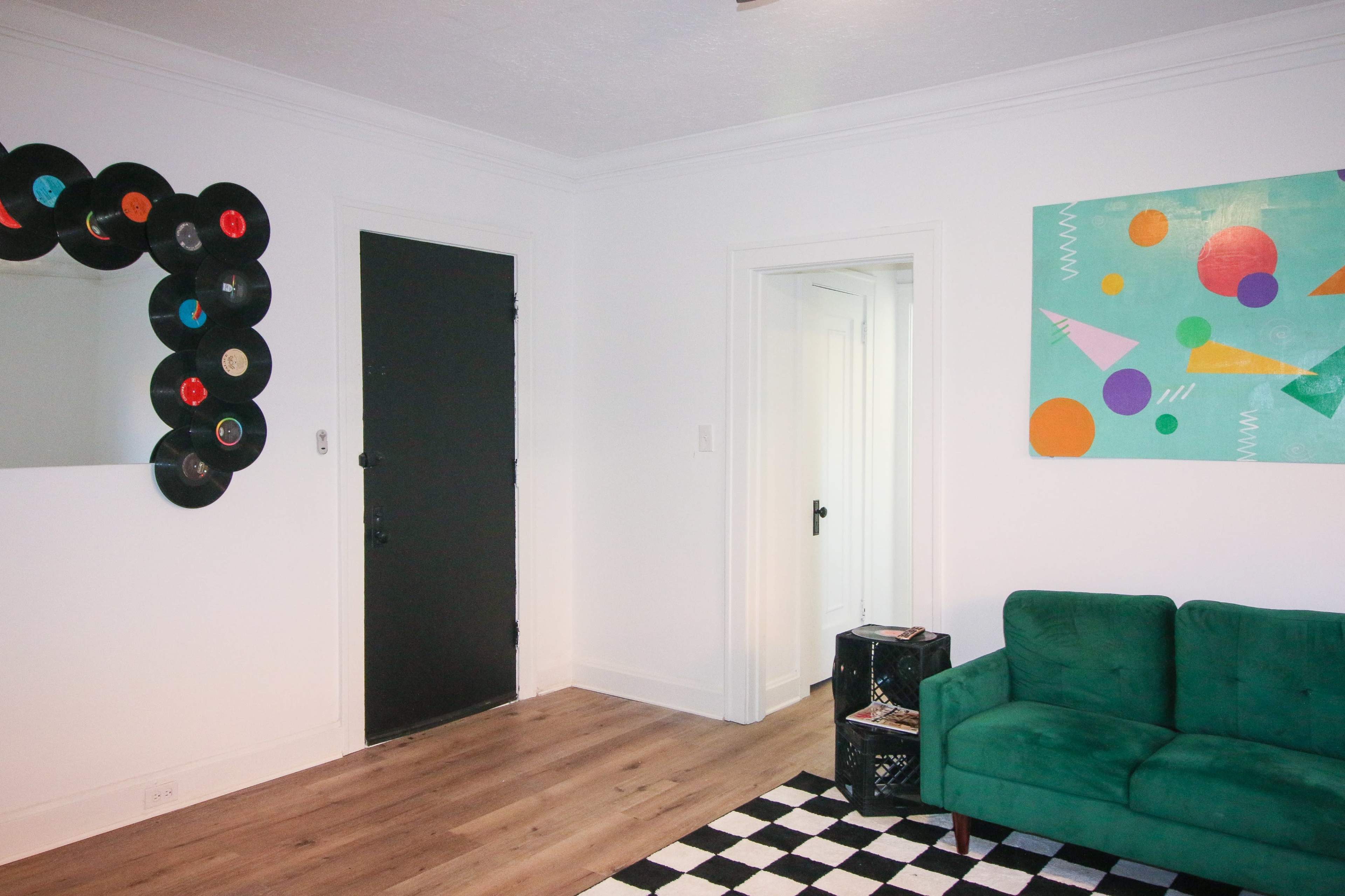 A modern room with a green sofa, a black door, a wall decorated with vinyl records, and an abstract art piece featuring colorful shapes.