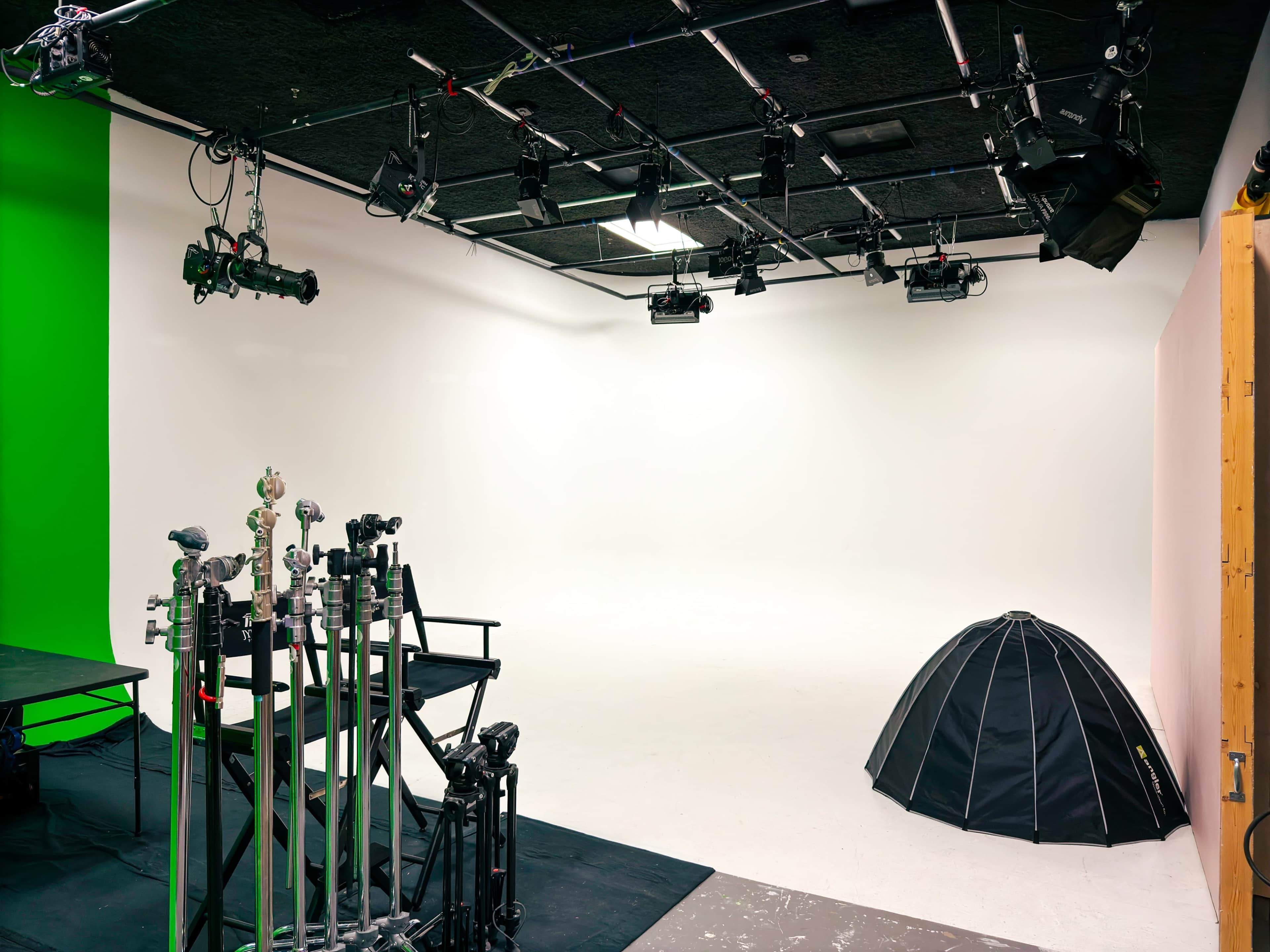 The image shows a spacious studio with a green wall, white floor, and various lighting equipment arranged on the ceiling.