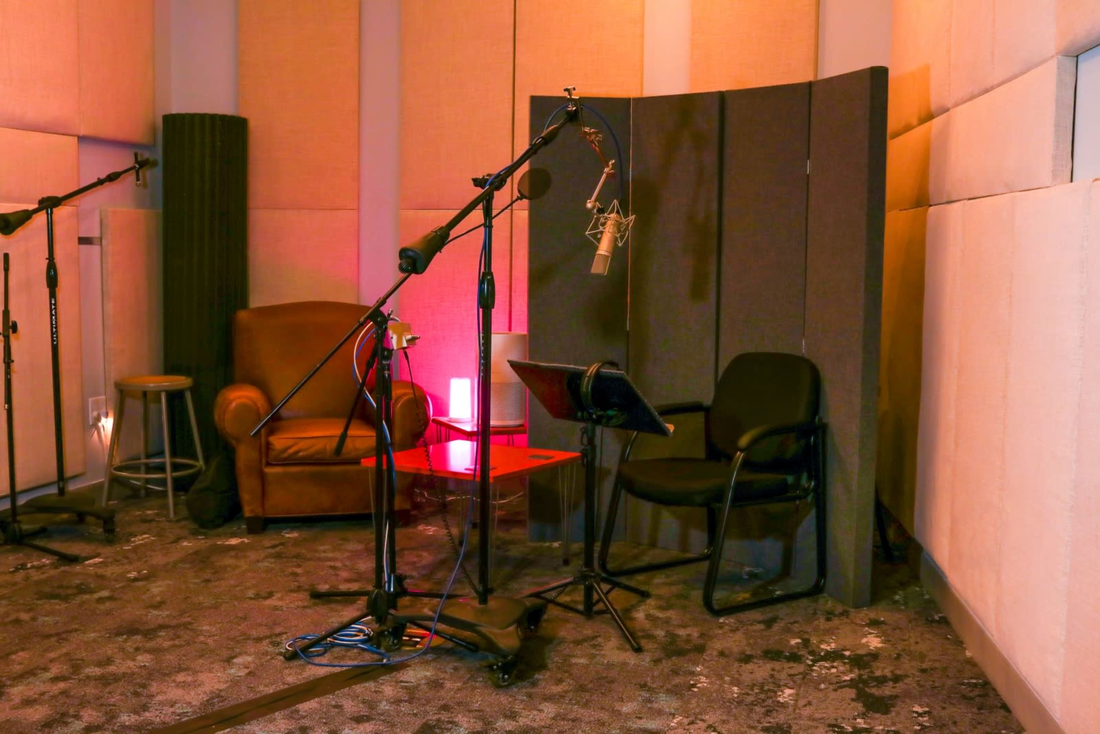 The image shows a sound recording studio with microphones set up near a brown armchair and a black chair.