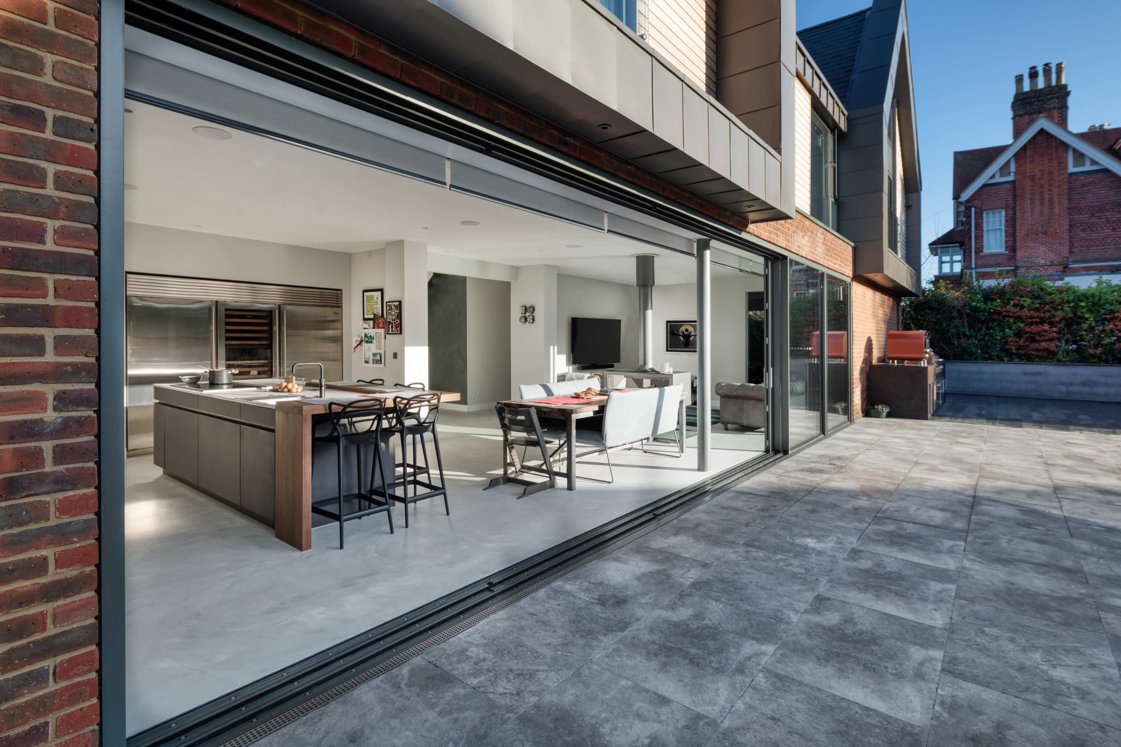 A modern, open-concept kitchen and dining area visible through large sliding glass doors, with a patio outside and a brick exterior.