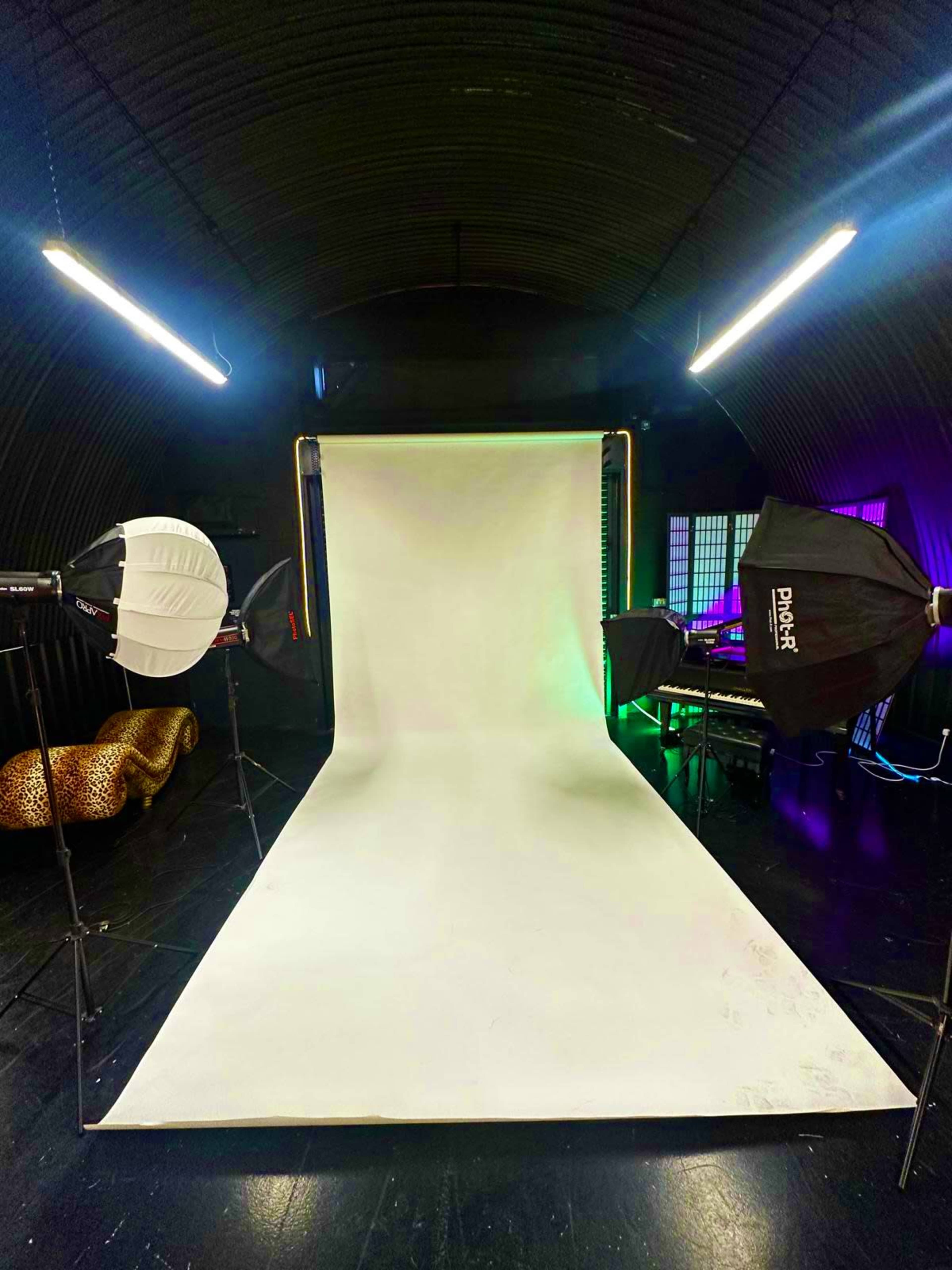 The image shows a photography studio setup with a white backdrop, studio lights positioned on either side, and a musical keyboard in the background.
