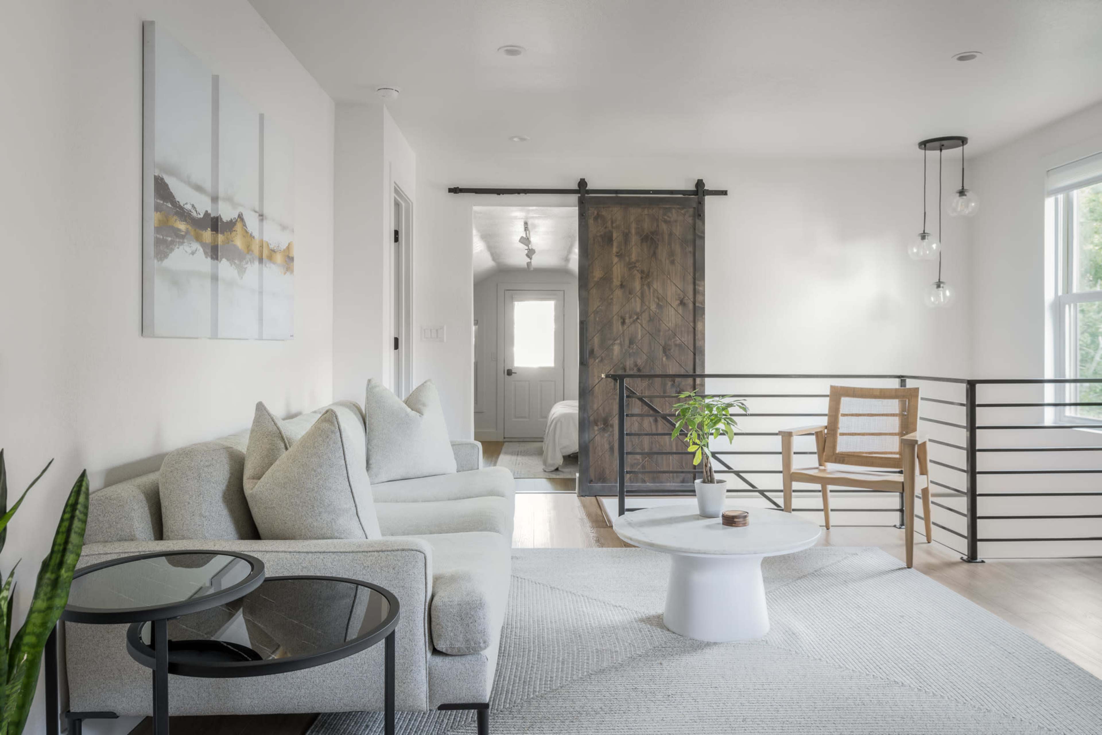 A modern living room with a light-colored sofa, a small round table, and a sliding barn door leading to a bedroom.