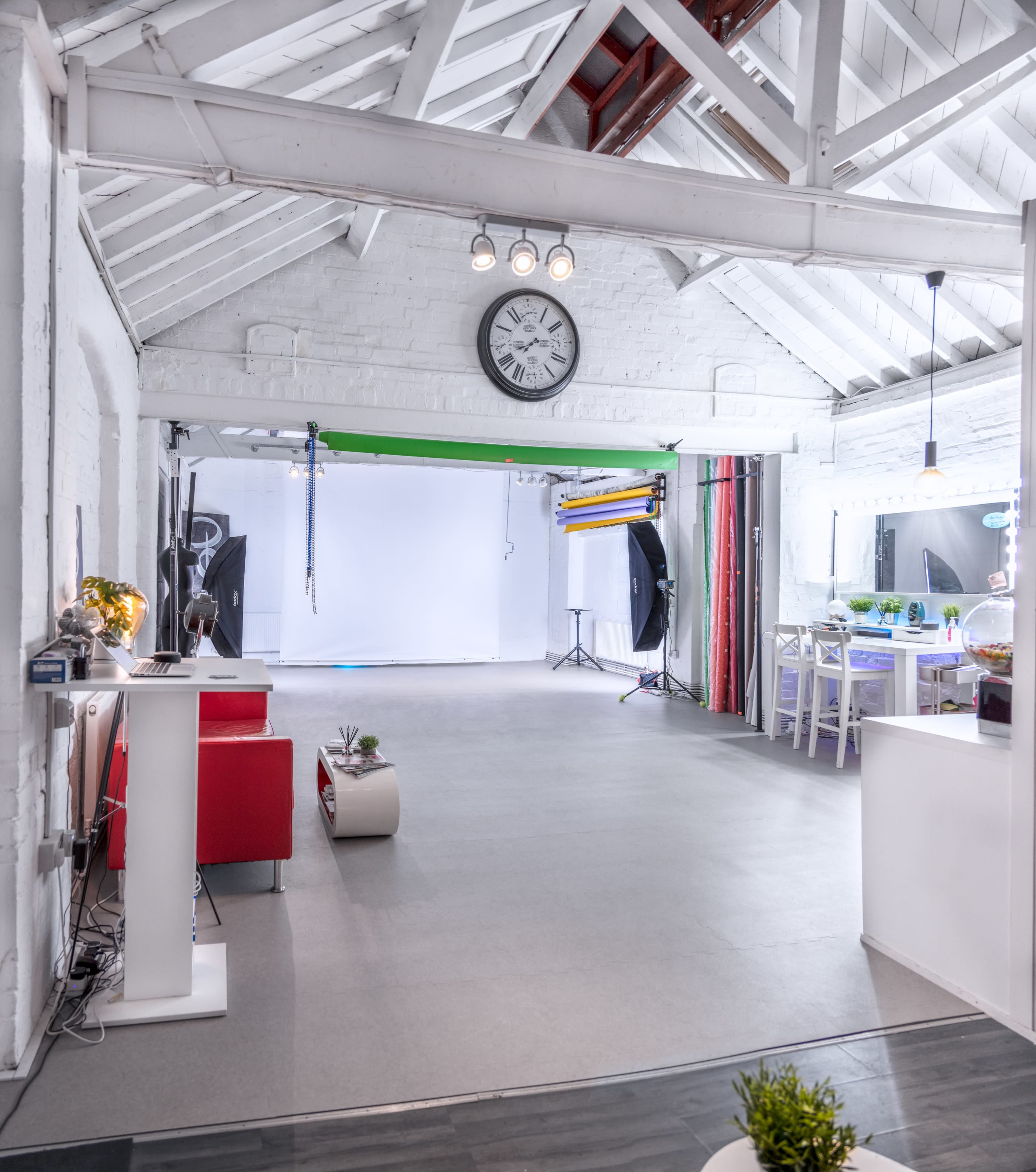 A well-lit photography studio with a large open area and various equipment, including a clock on the wall and a desk with a computer.