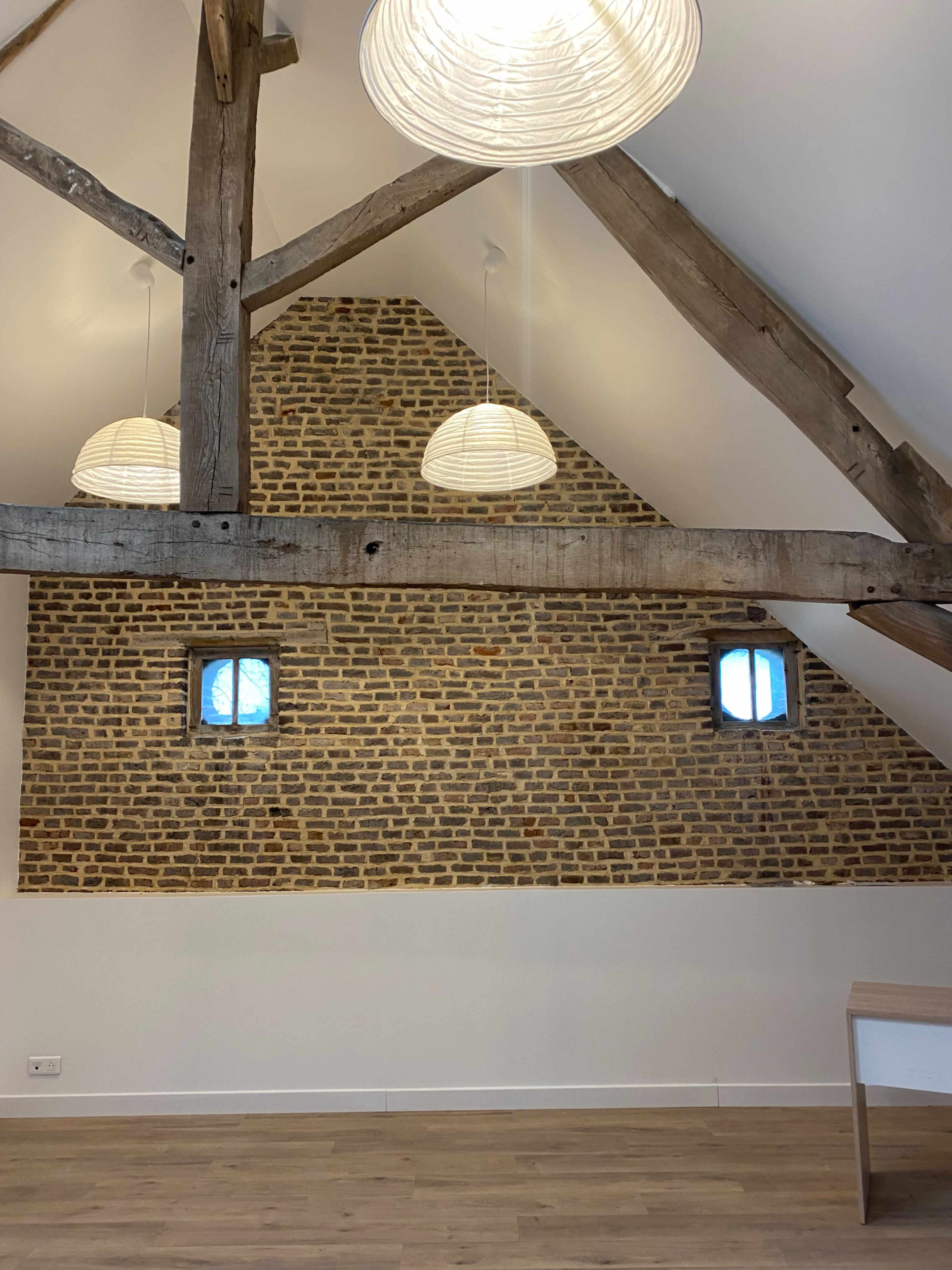 The image shows an attic with exposed wooden beams, a brick wall, and two round pendant lights hanging from the ceiling.
