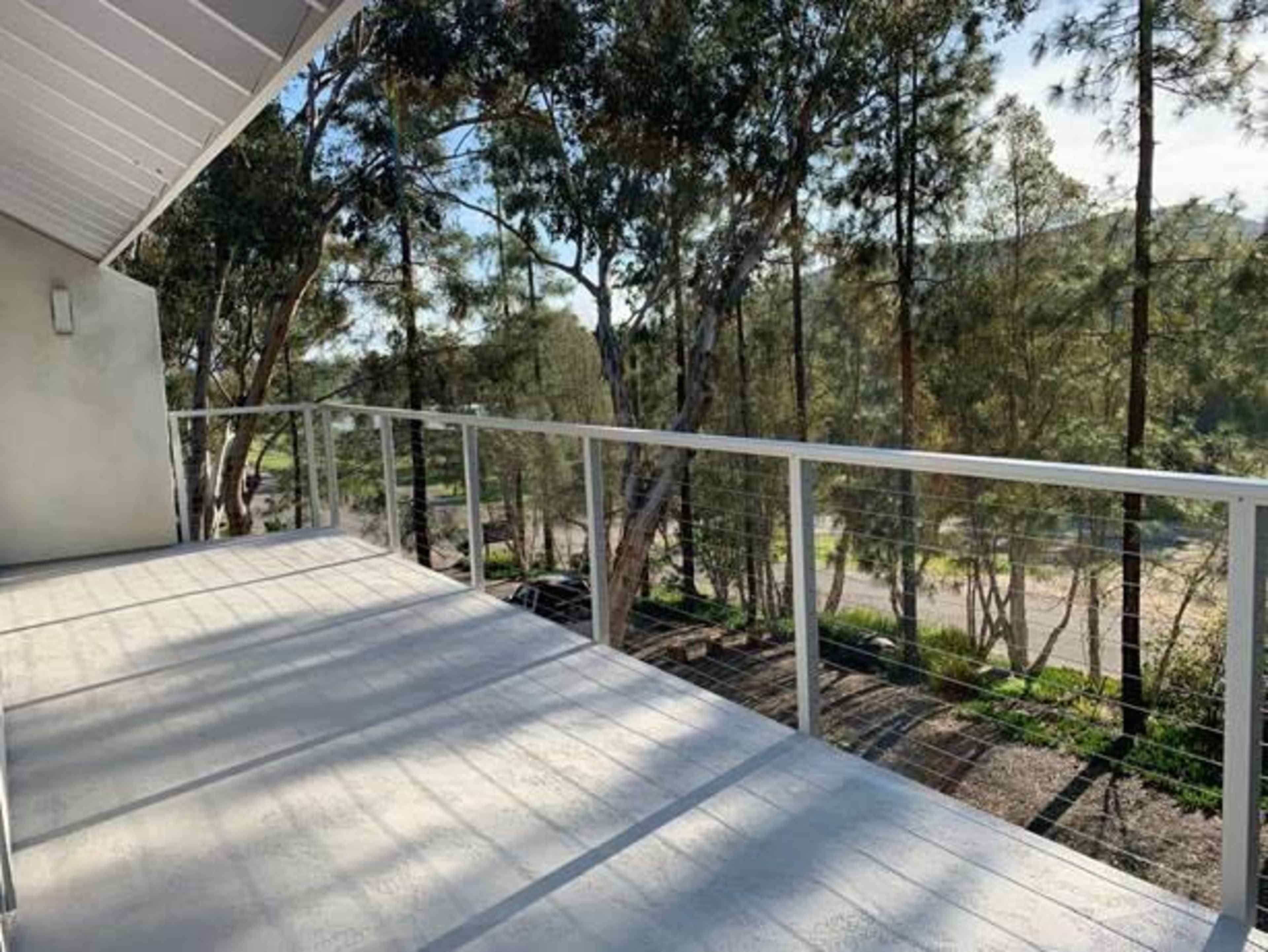 The image shows a clear balcony with a metal railing overlooking a forested area.
