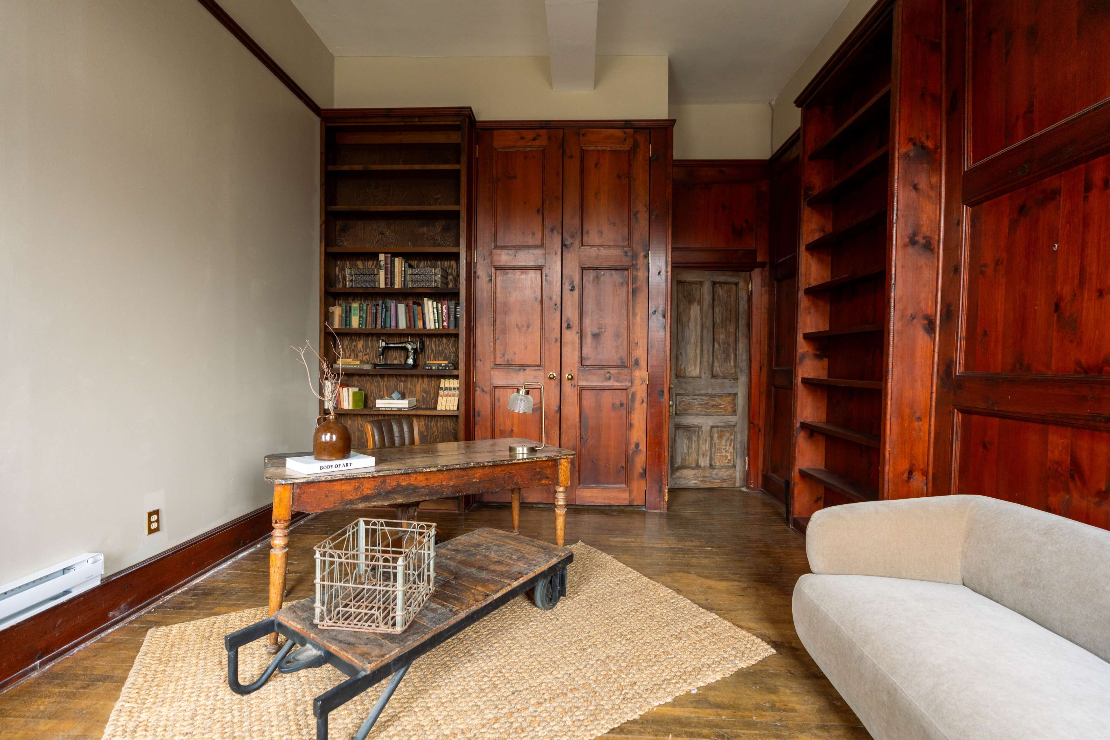 The image shows a room with wooden walls, a central table, a beige couch, and bookshelves filled with books.
