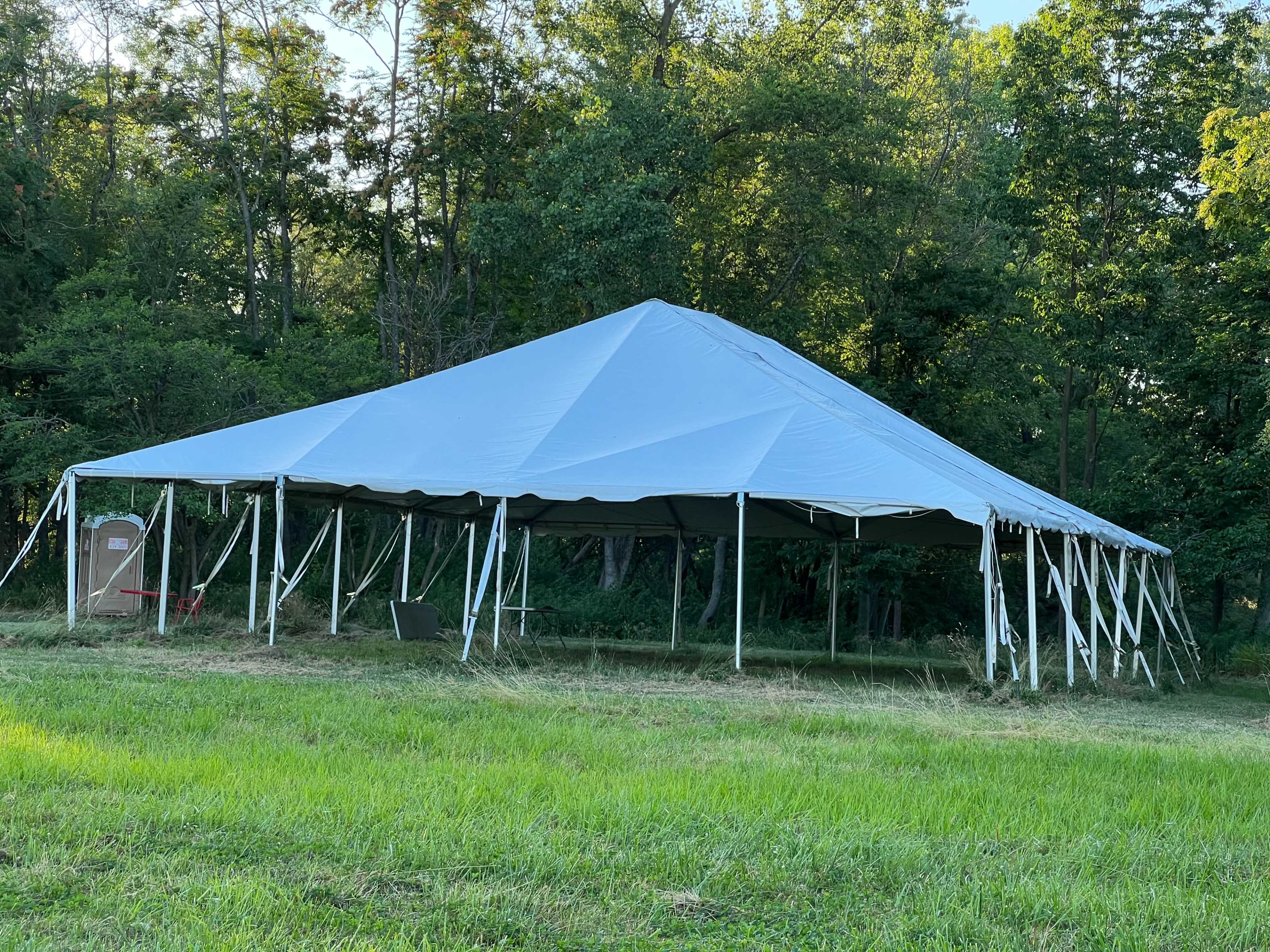 A large white tent is set up on a grassy area surrounded by trees.