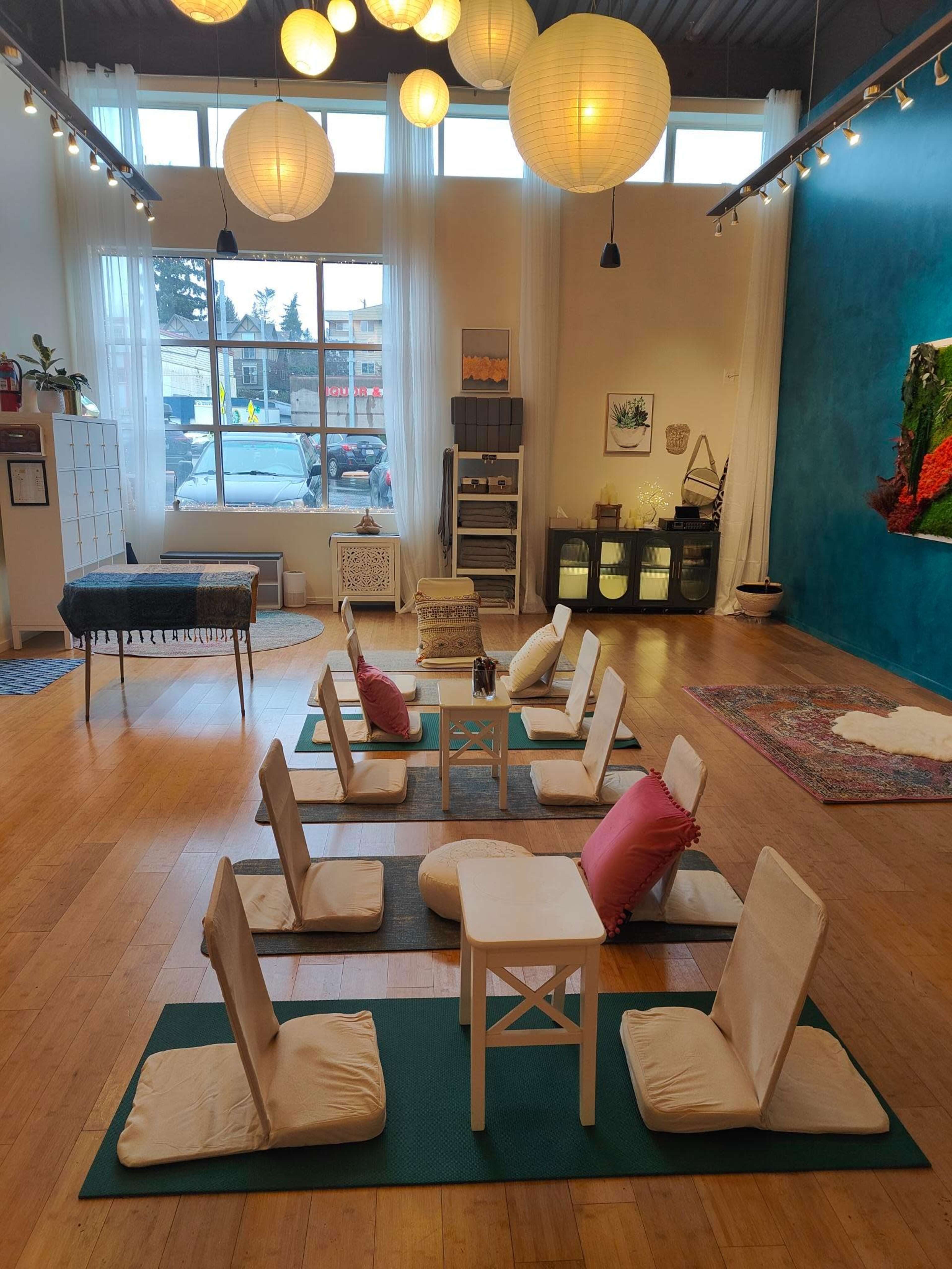 A spacious room arranged with low seating pads around small tables, illuminated by hanging lanterns and featuring a blue accent wall.