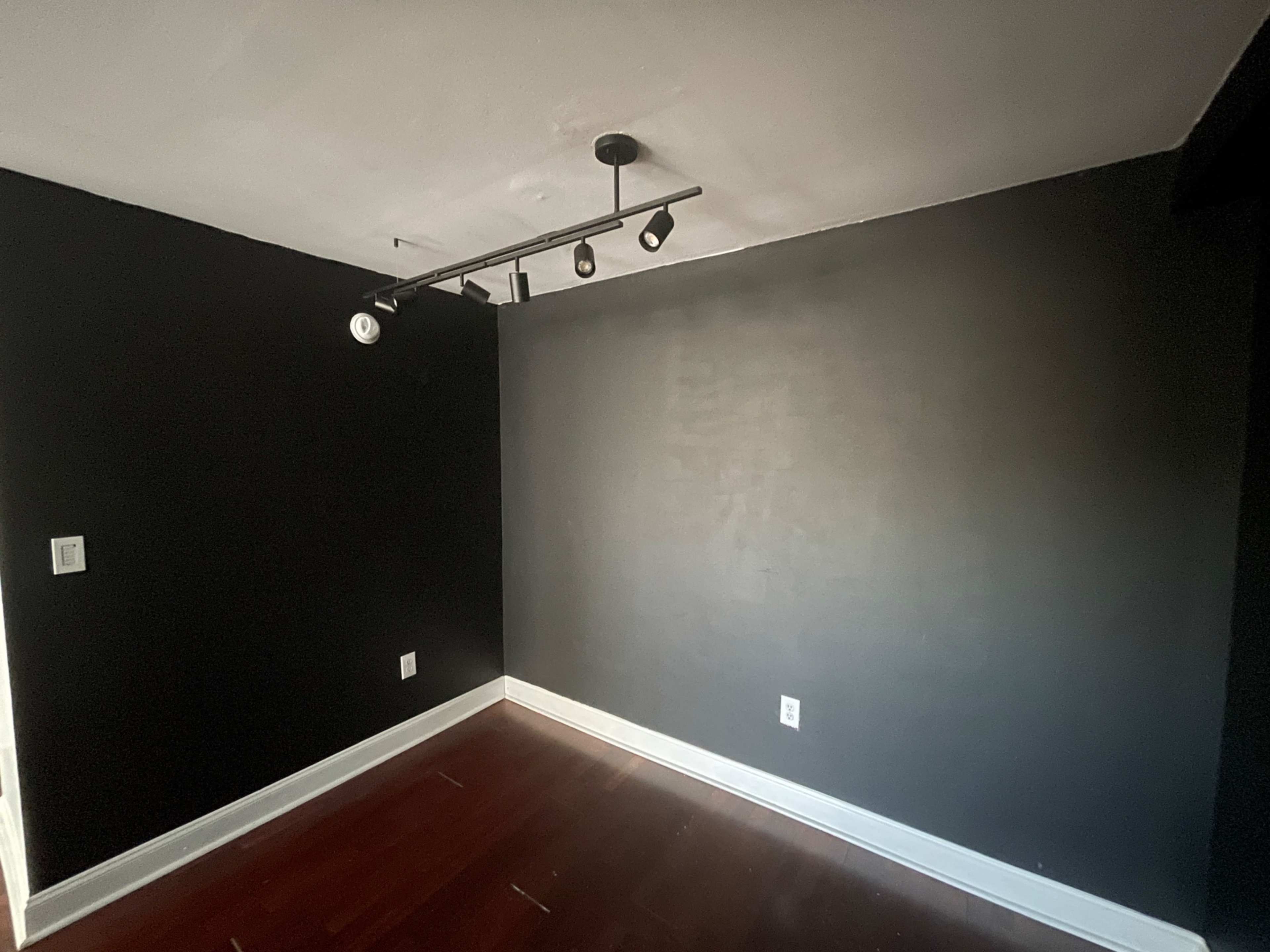 A room with a black wall, a spotlight track lighting fixture, and hardwood flooring.
