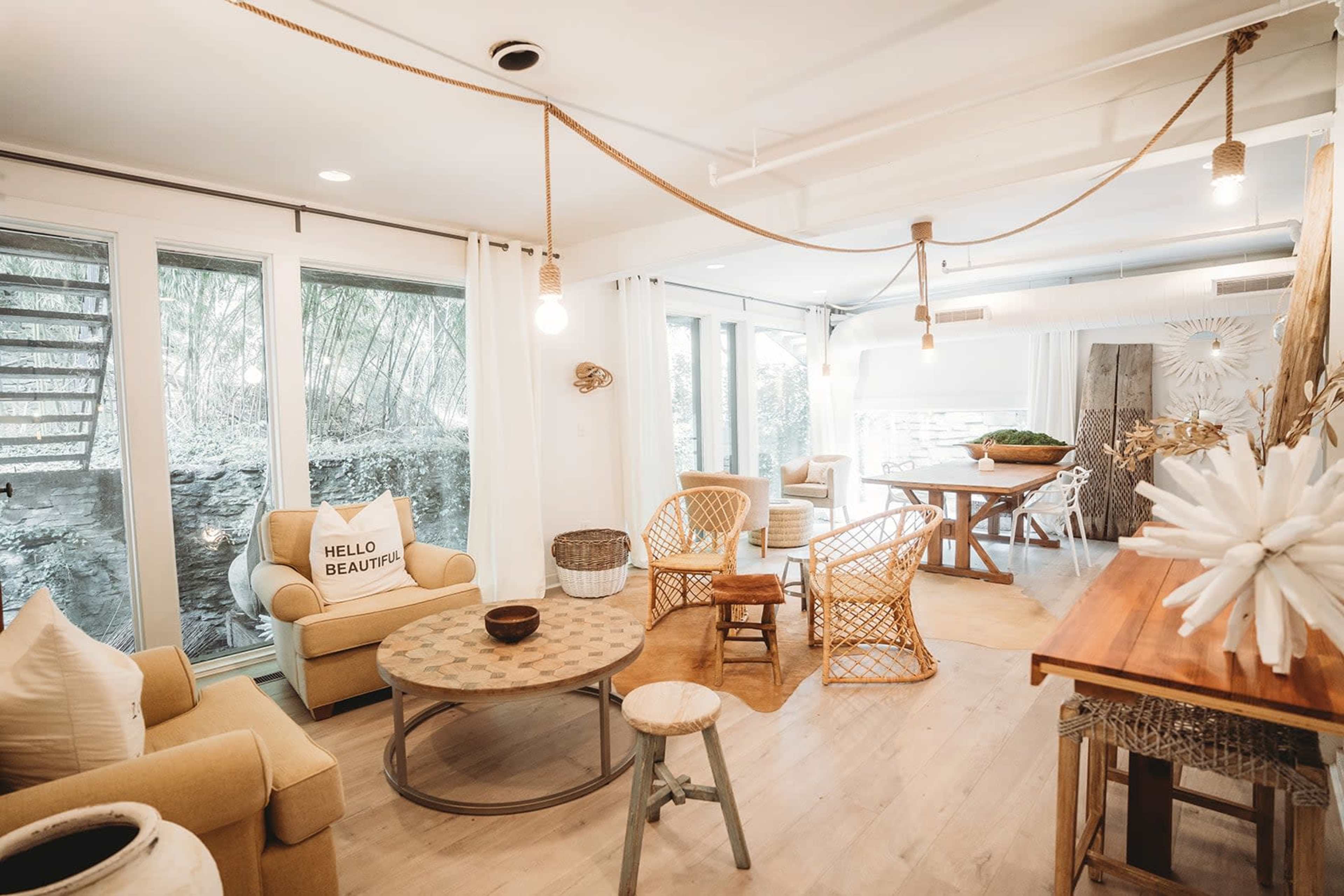 A cozy living space with a mix of wicker and upholstered furniture, a large table, and large windows allowing natural light to enter.
