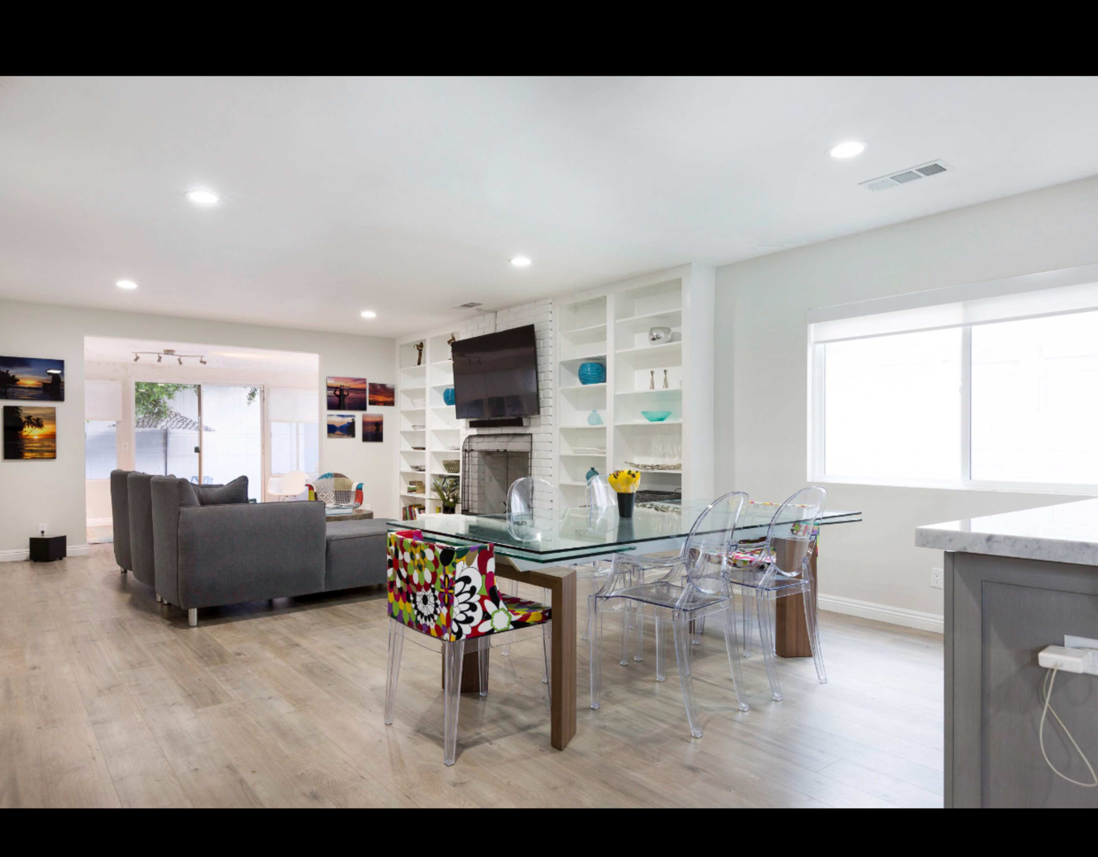 A modern living room and dining area with a gray sofa, a glass dining table surrounded by clear chairs, and built-in shelves displaying decorative items.