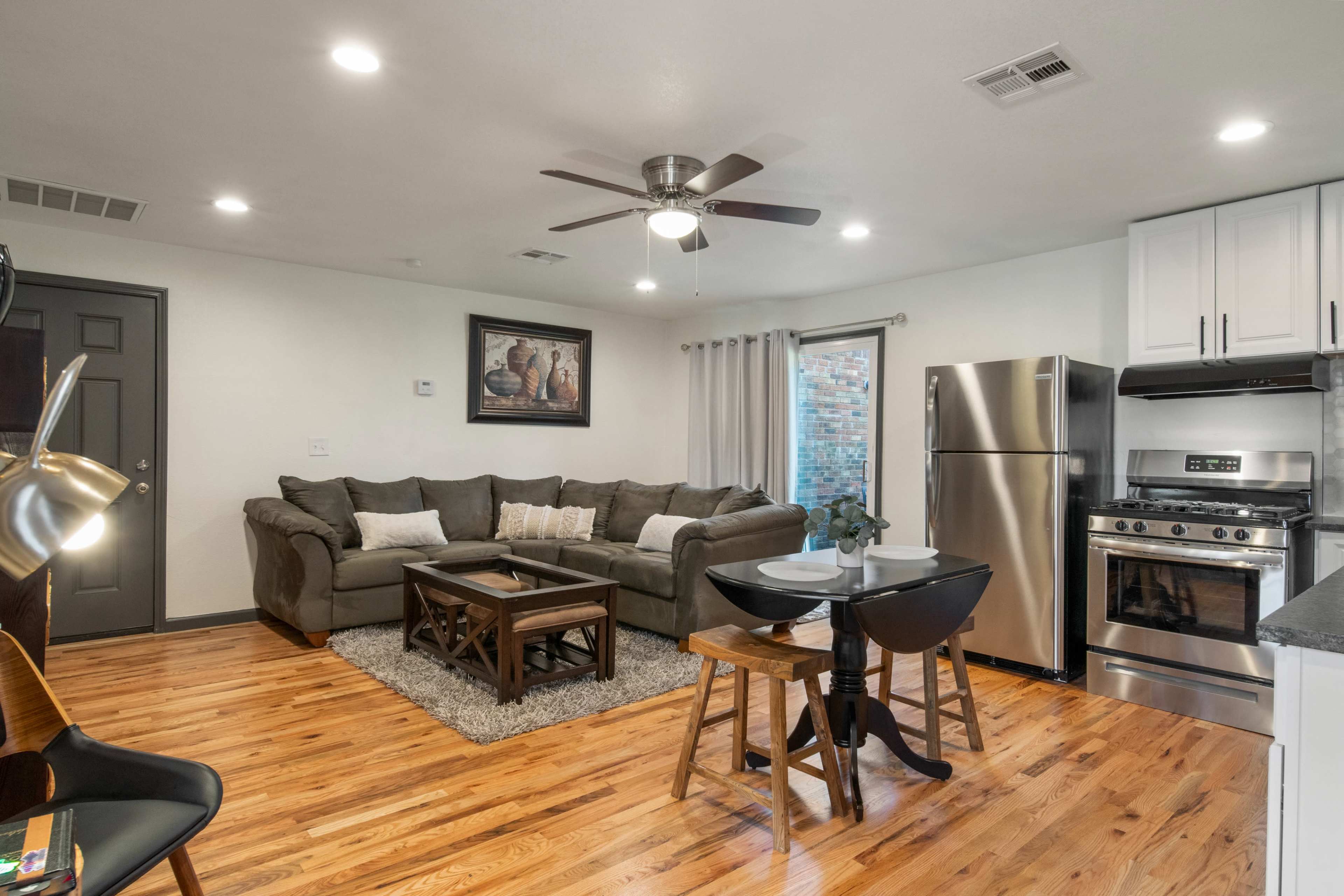 A cozy living area features a sectional sofa, a wooden coffee table, a dining table with two chairs, and a modern kitchen with stainless steel appliances.
