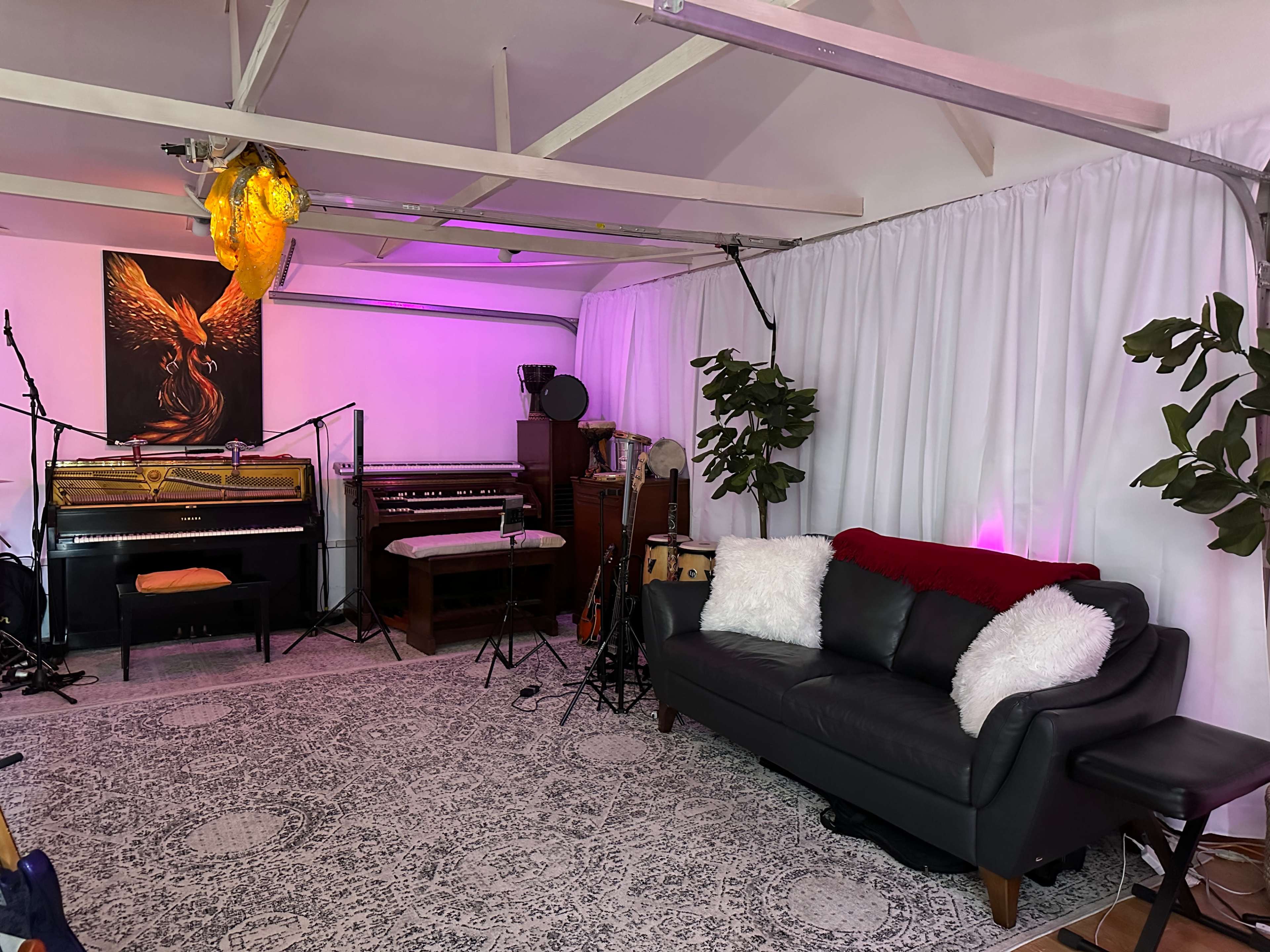 A cozy music rehearsal space featuring two pianos, a couch with decorative pillows, and indoor plants under soft lighting.