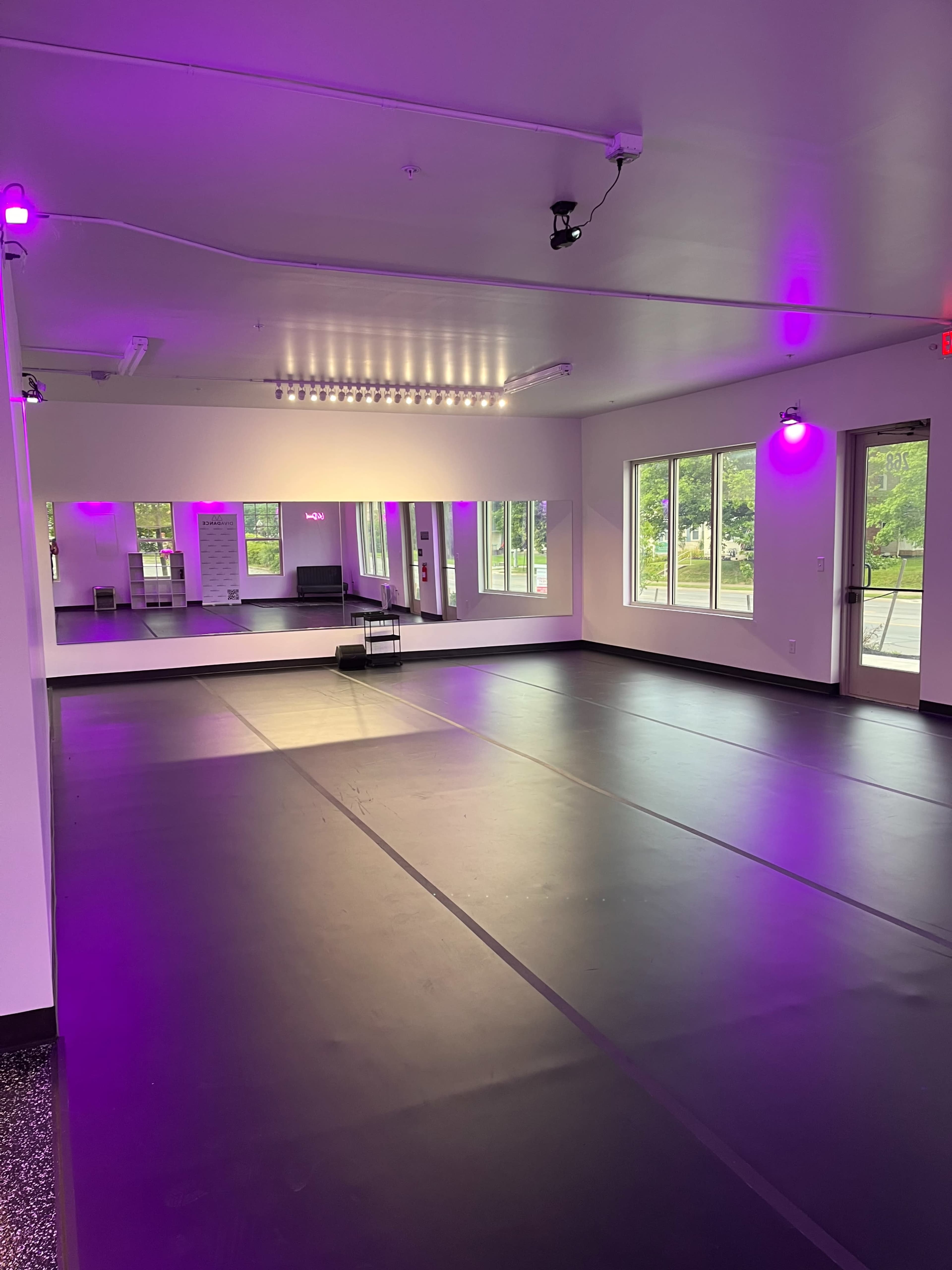 The image shows a spacious studio with a black floor, large windows, and purple lighting.