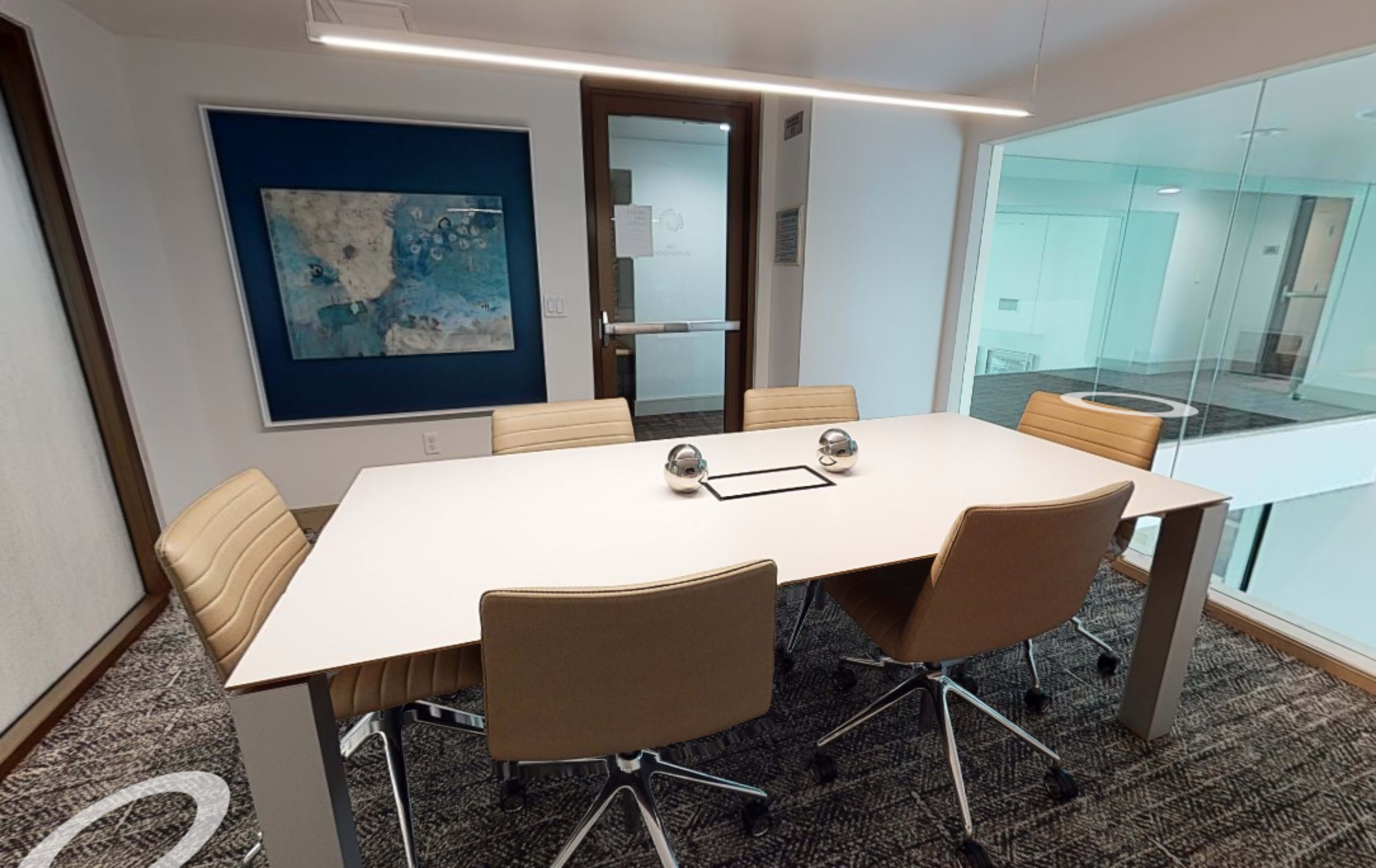 A modern conference room with a white table surrounded by four beige chairs, and an abstract painting on the wall.