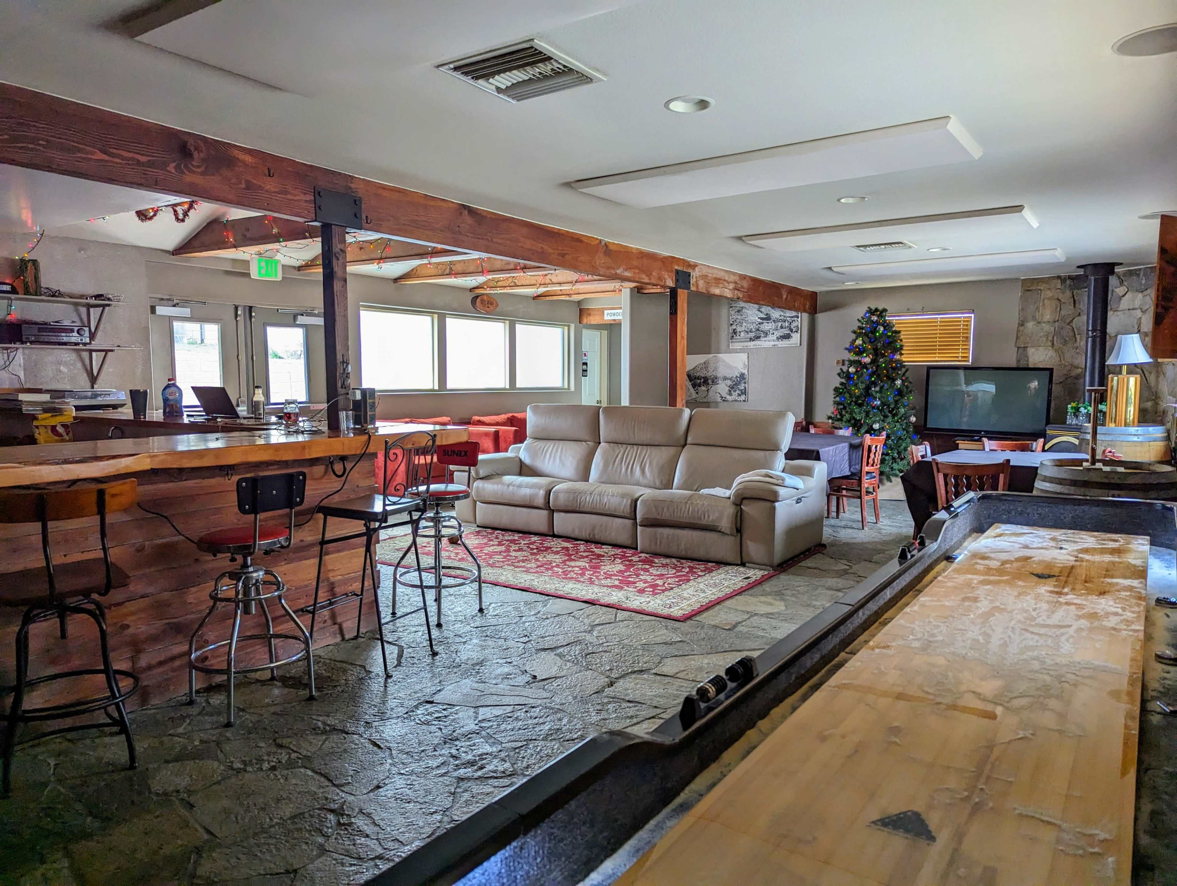 A spacious interior with a bar area, a cozy couch in the center, and a Christmas tree in the corner.