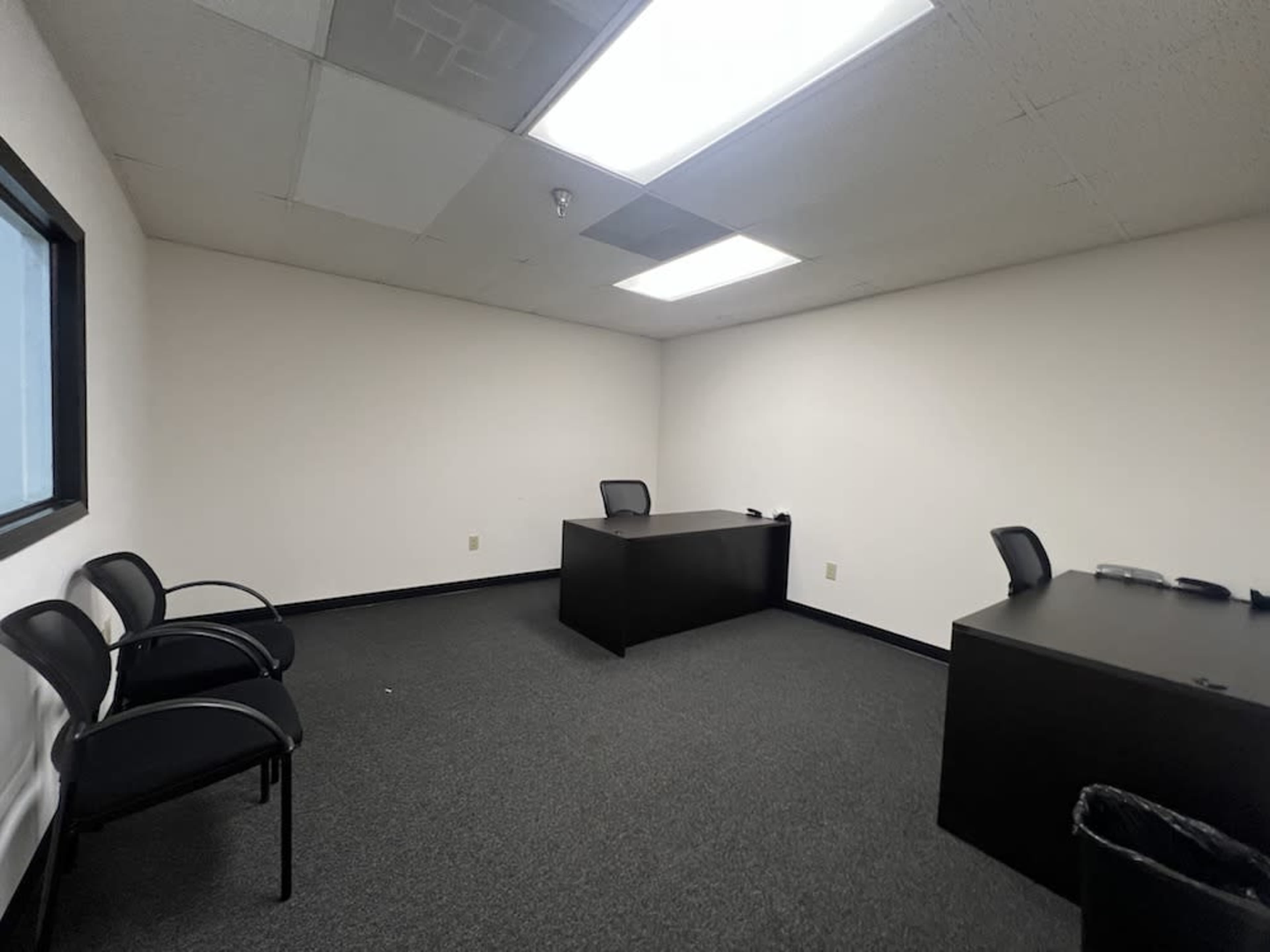 The image shows an empty office space featuring a desk, two chairs, and a window on one wall.