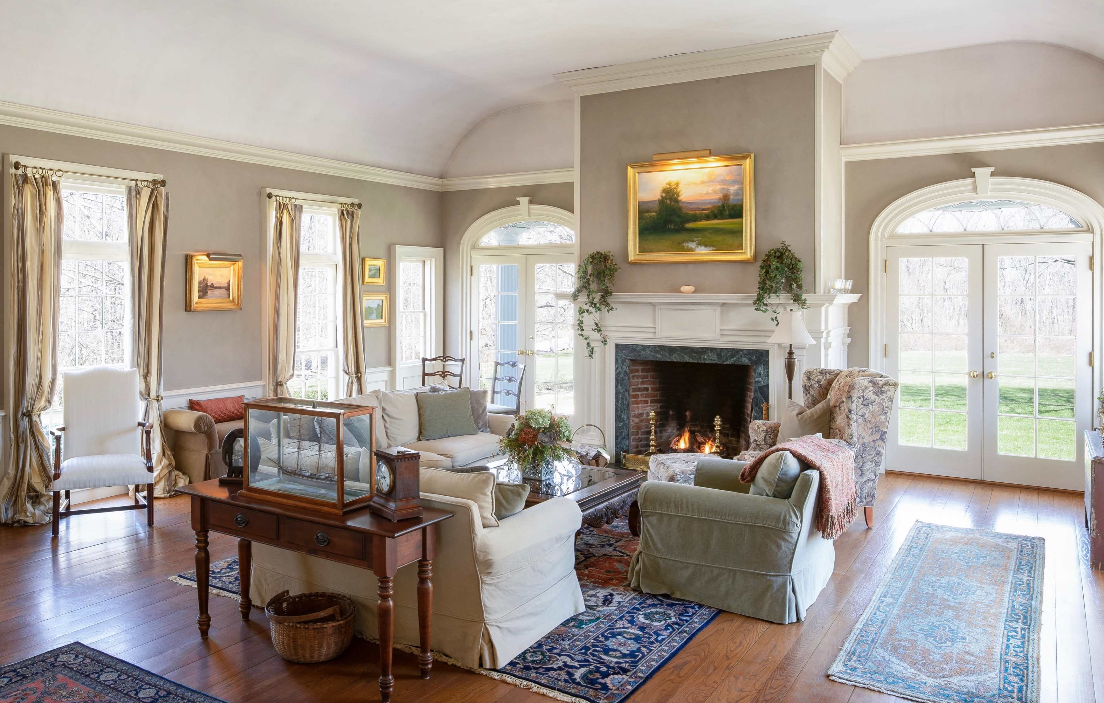 A light-filled living room features a fireplace, comfortable seating, and large windows overlooking a grassy yard.