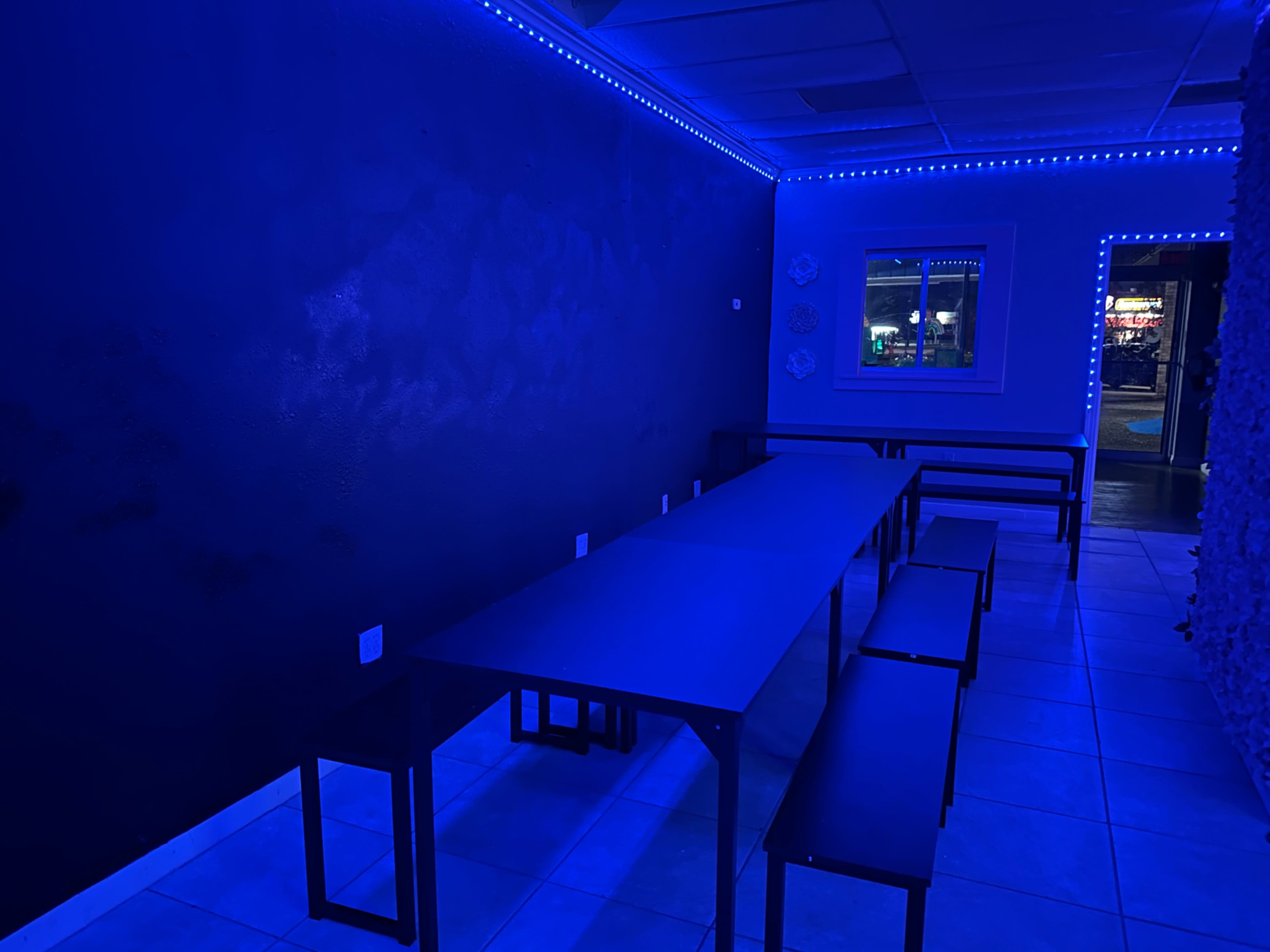 A dimly lit room features a long table surrounded by benches, illuminated by blue LED lights along the walls.