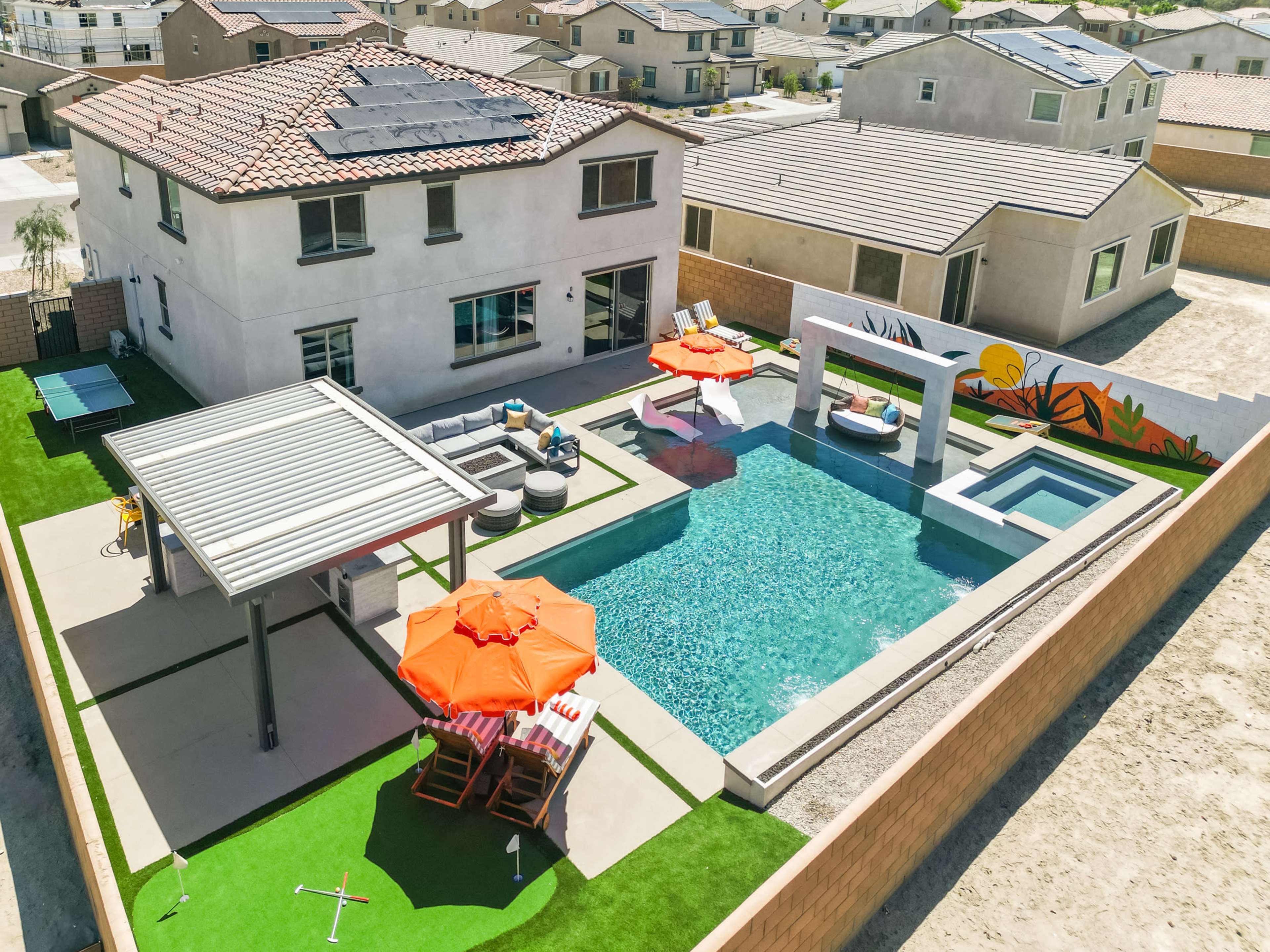 The image shows a modern backyard with a swimming pool, spa, outdoor seating area, and umbrellas, surrounded by houses in a residential neighborhood.