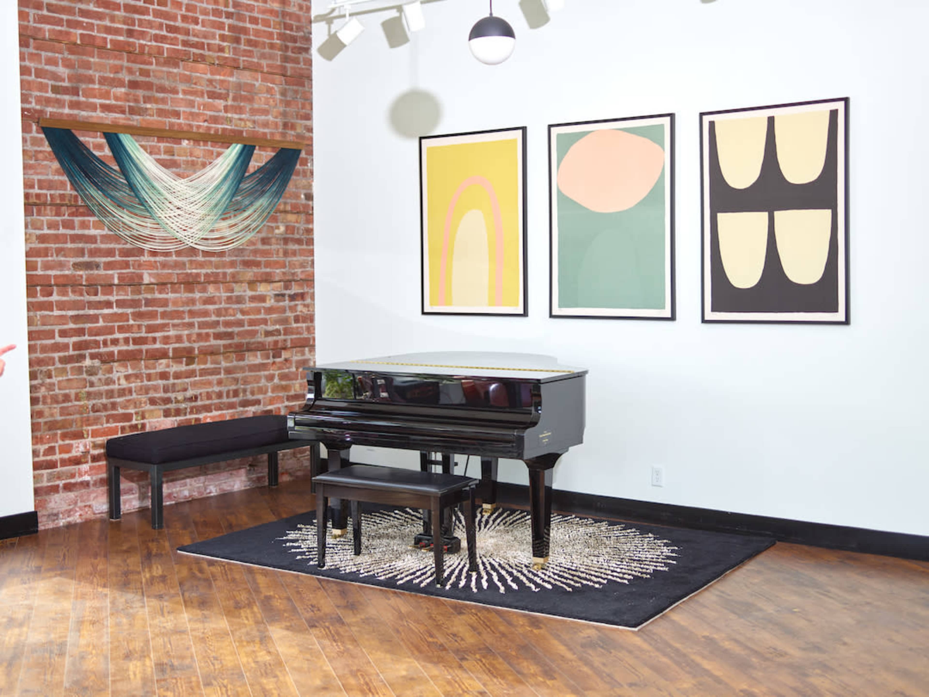 A black piano sits on a circular rug in a room with exposed brick walls and framed abstract art.