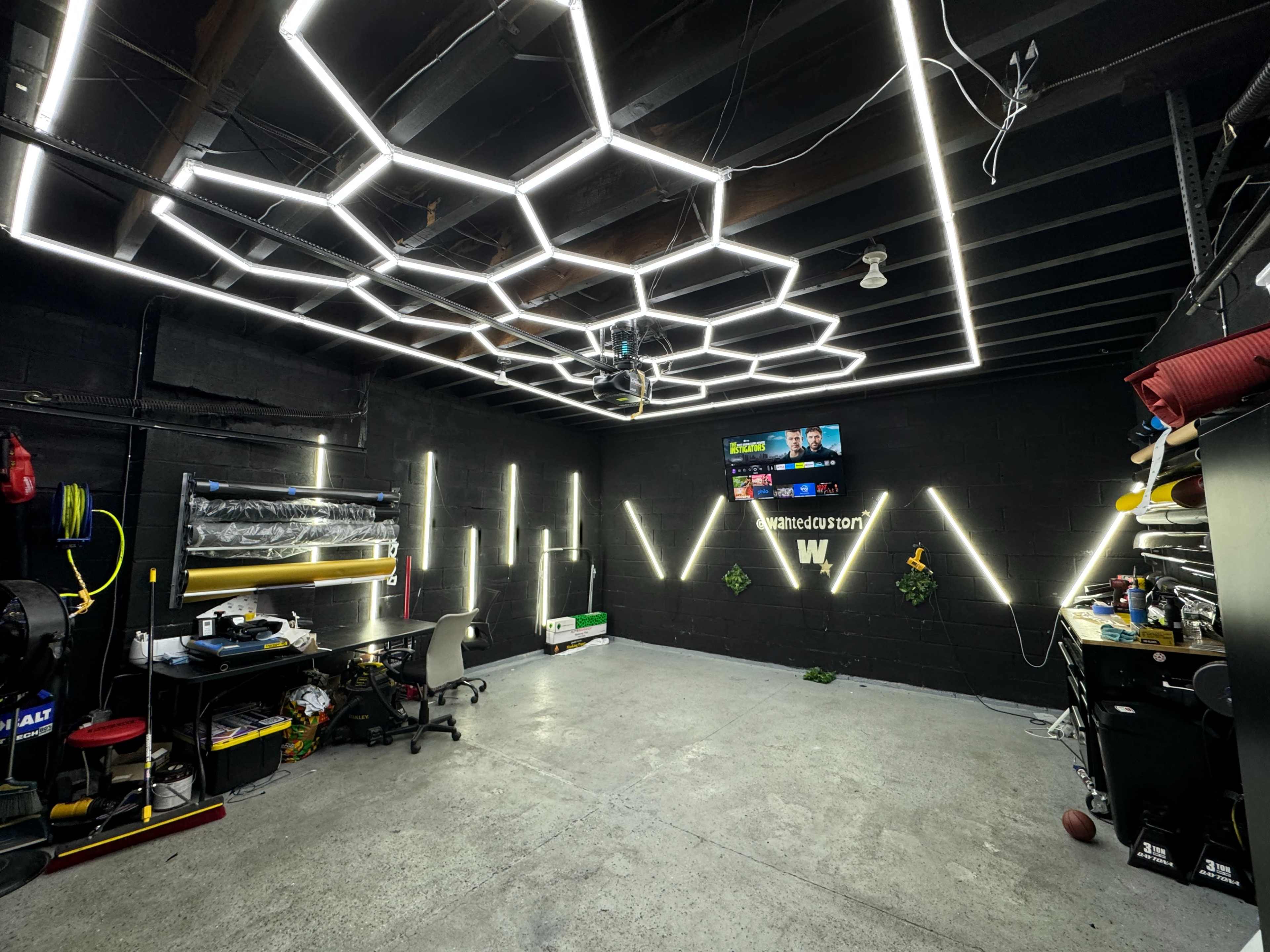 A modern workspace with a hexagonal LED light ceiling, black walls, and various tools and equipment arranged on work tables.