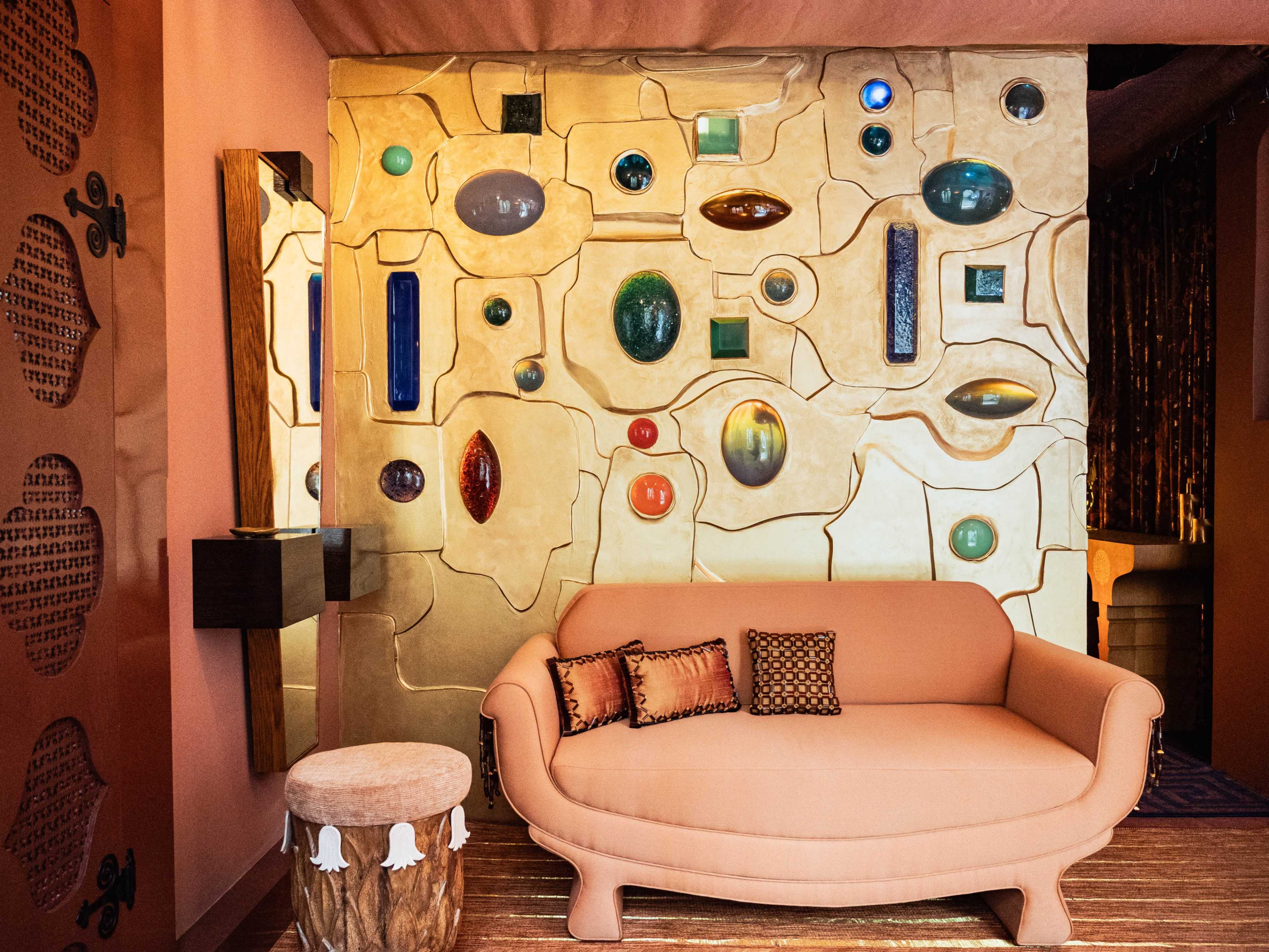The image features a uniquely designed room with a light-colored wall adorned with various colored glass elements and a curved peach-colored sofa.