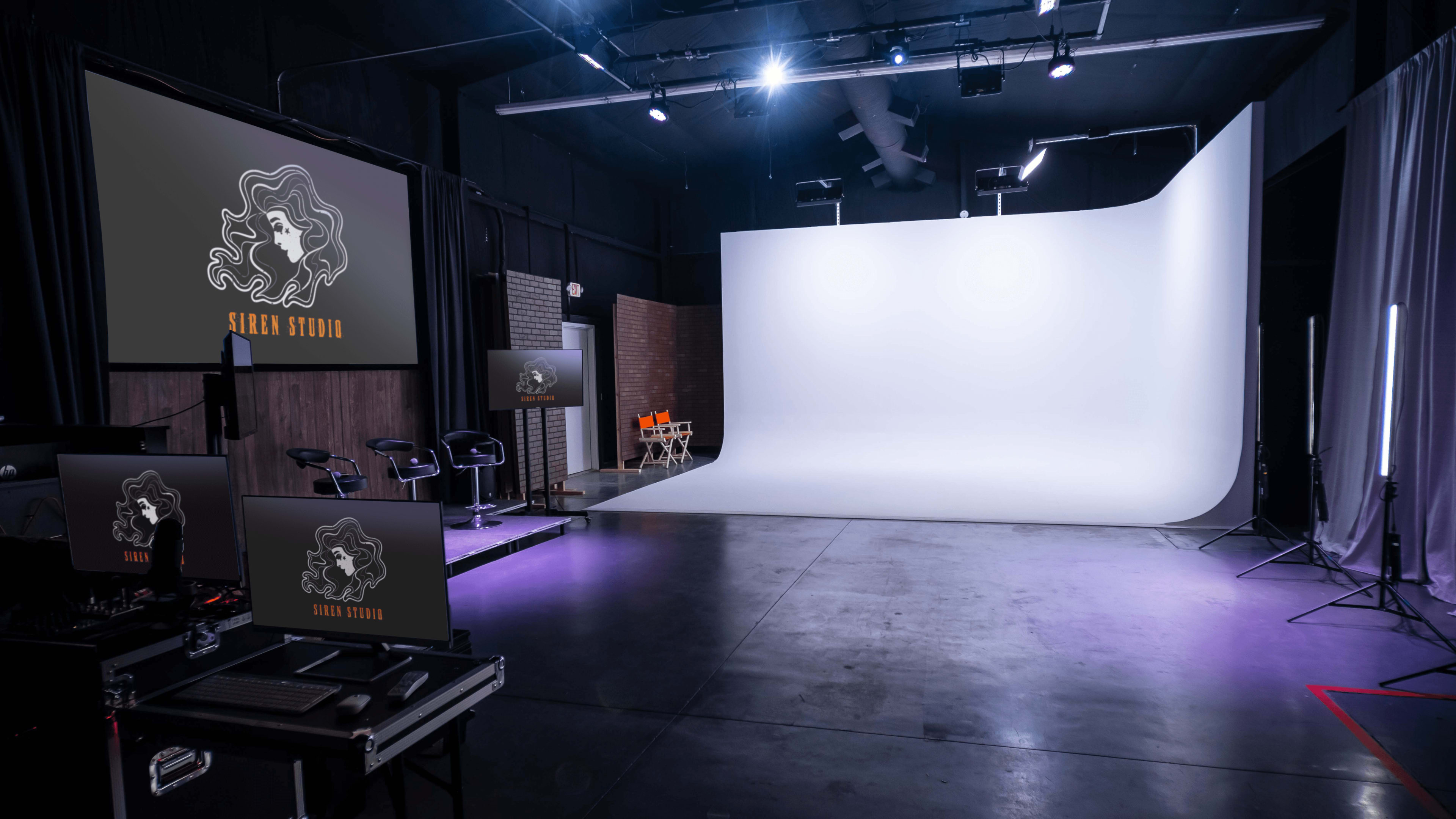 A photography studio features a large white backdrop, multiple computer screens displaying the "Siren Studio" logo, and seating arranged in front of the backdrop.