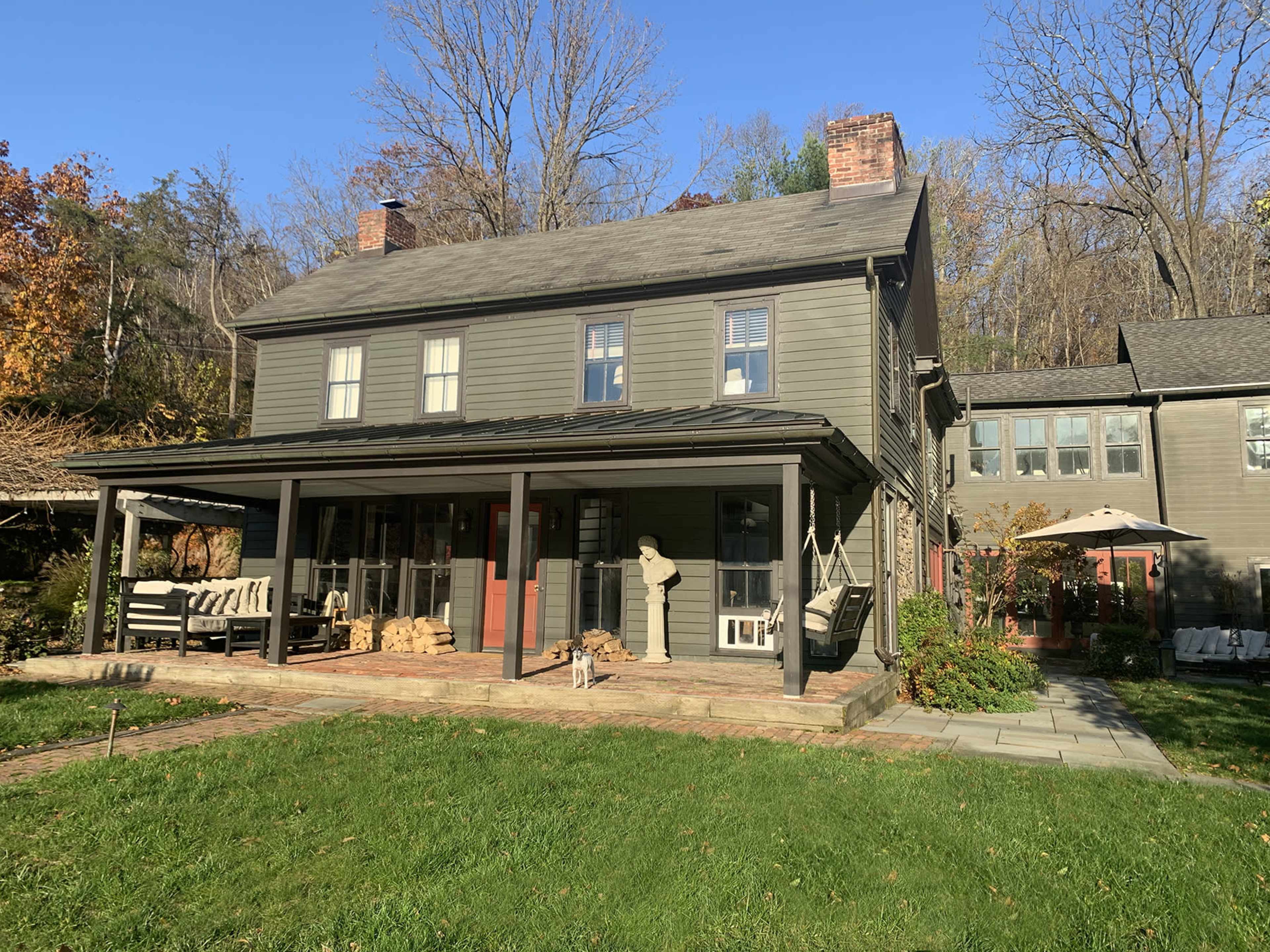 A two-story gray house with a front porch and a yard, surrounded by trees and shrubs.