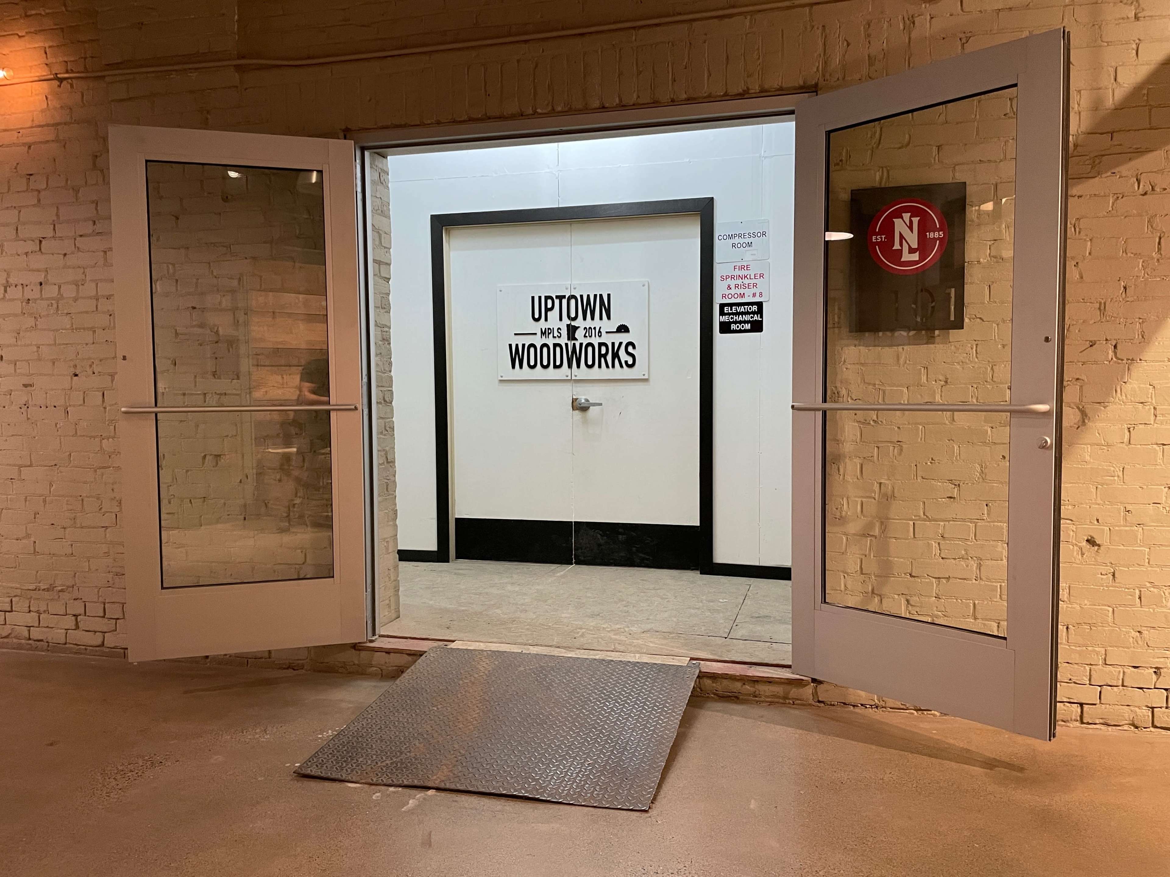 The image shows double doors open to a hallway with a sign that says "UPTOWN WOODWORKS" on the wall opposite the entrance.