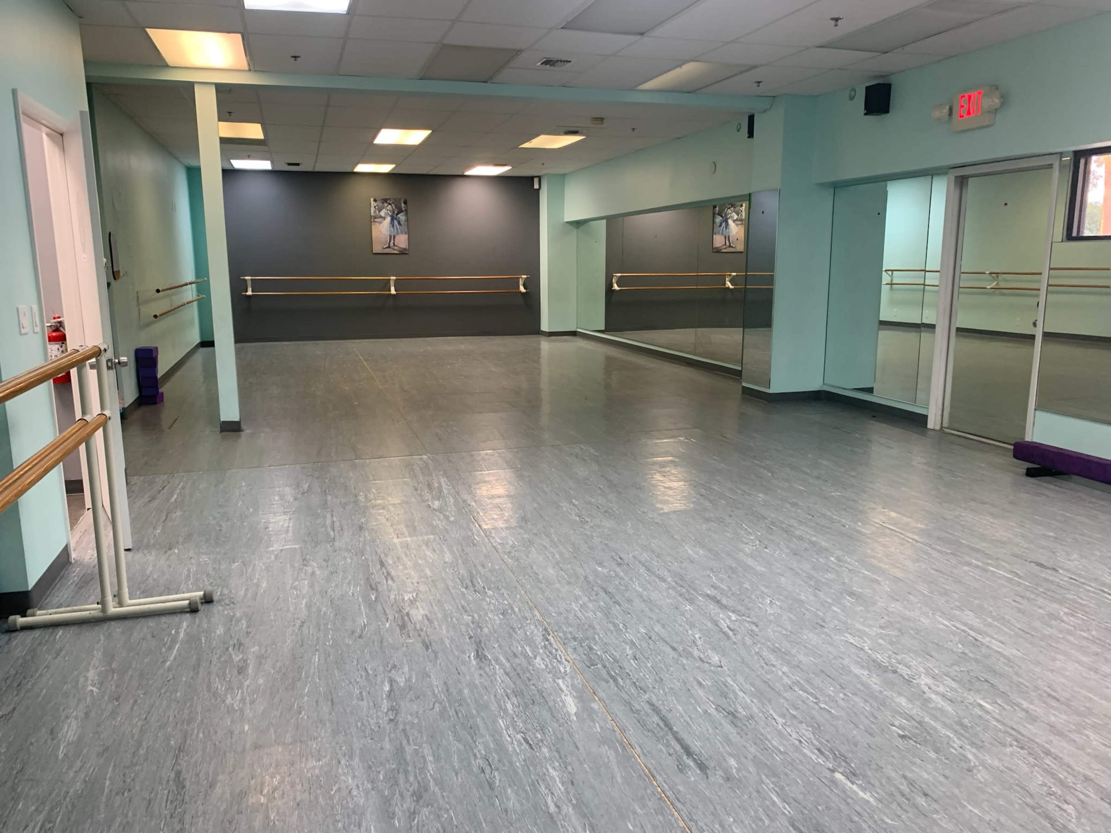 An empty dance studio with mirrored walls, ballet bars, and a light blue color scheme.