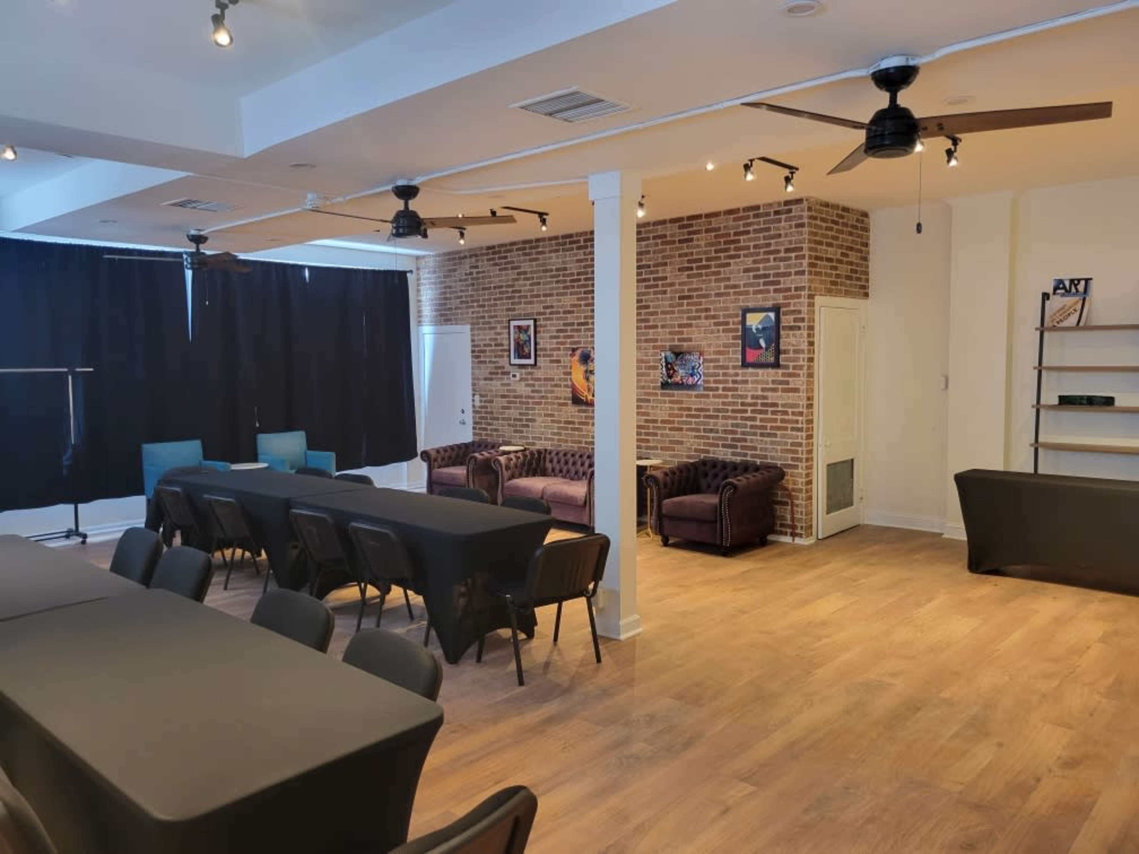 A spacious room with a seating area featuring two sofas, tables arranged with black covers, and a brick wall adorned with framed artwork.