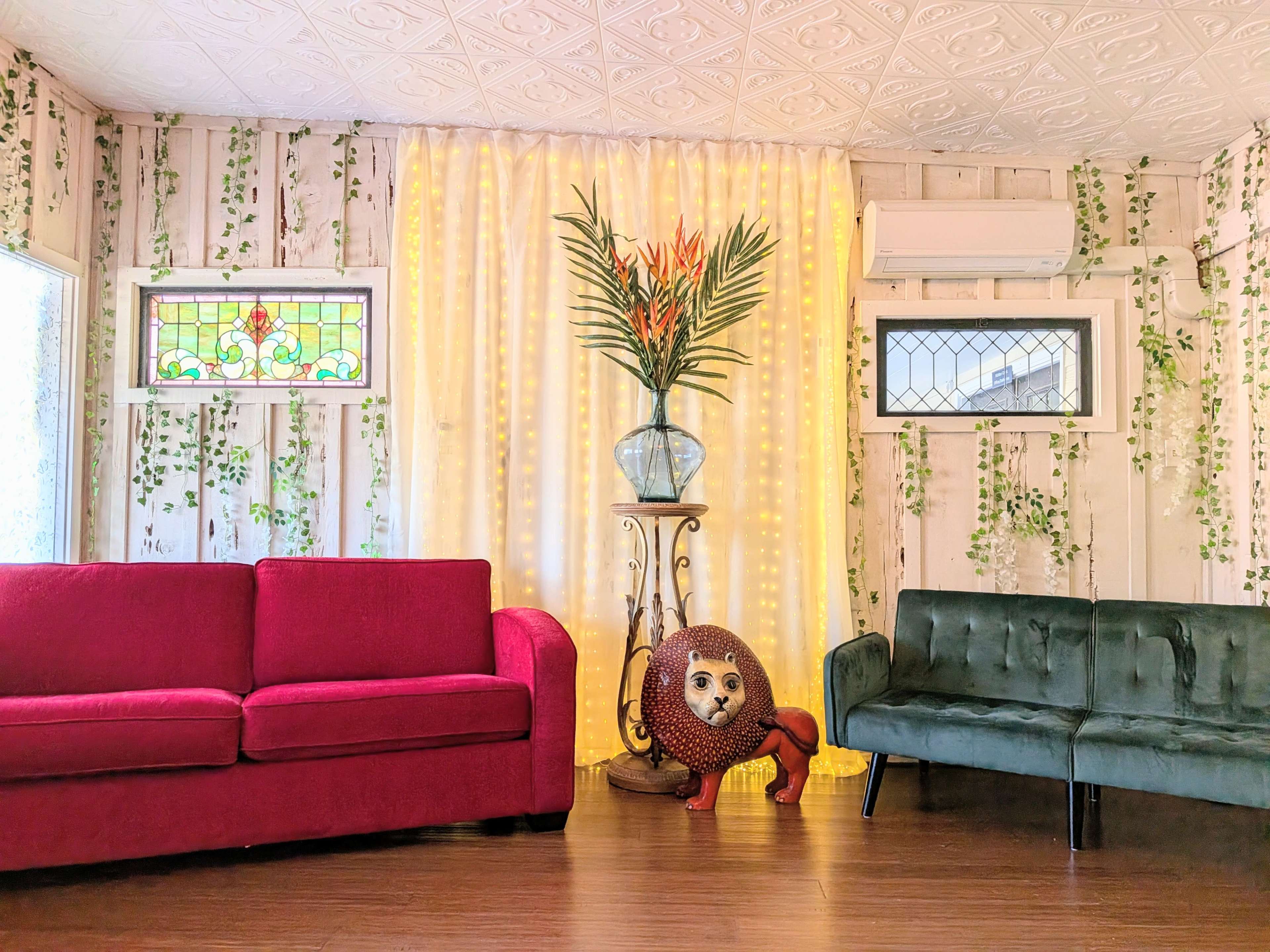 The image shows a brightly lit room with two sofas, one pink and one green, and a decorative lion-shaped planter holding tropical plants in the center.
