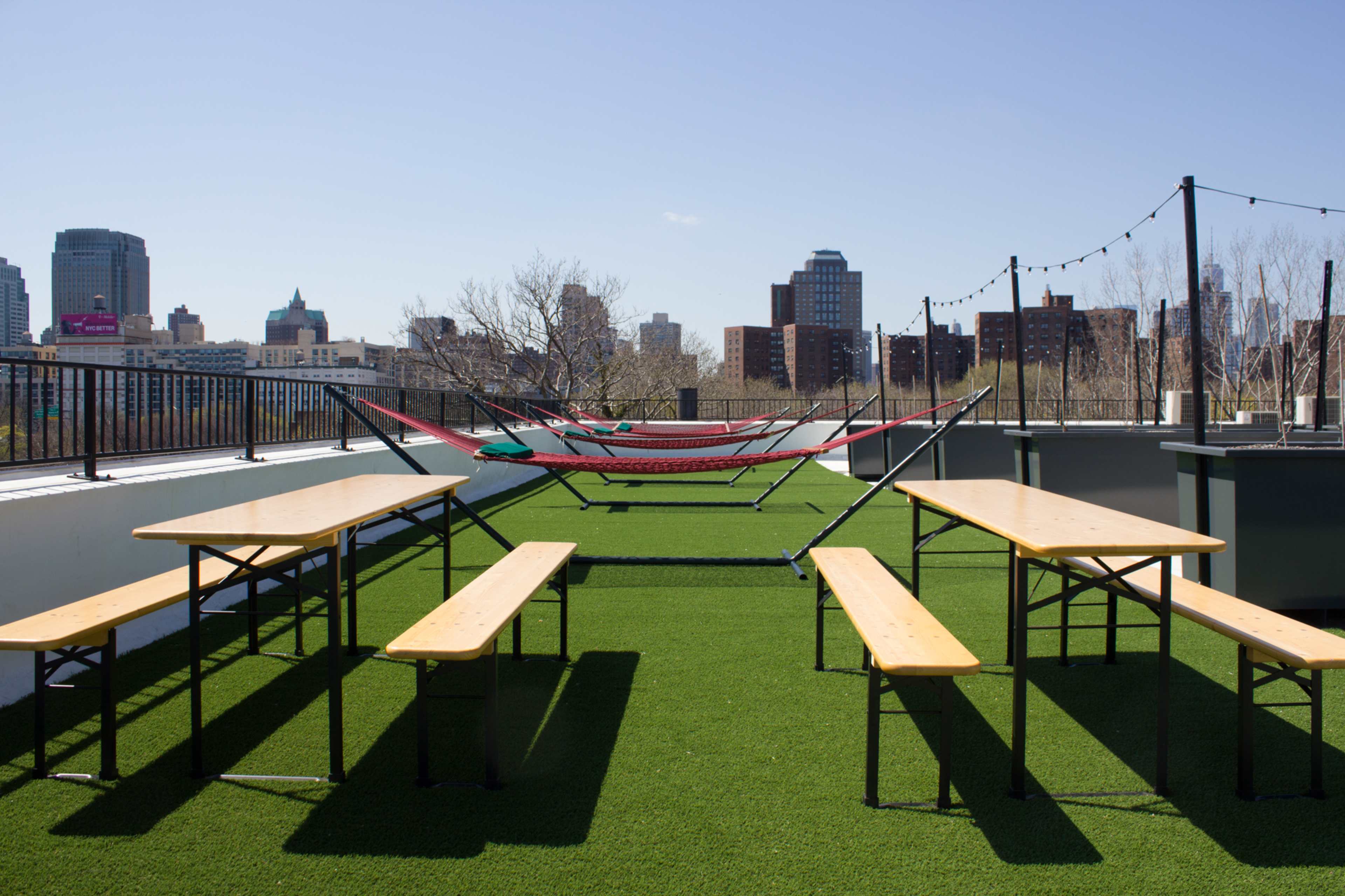 A rooftop terrace with two red hammocks suspended between posts and several wooden picnic tables set on artificial grass.