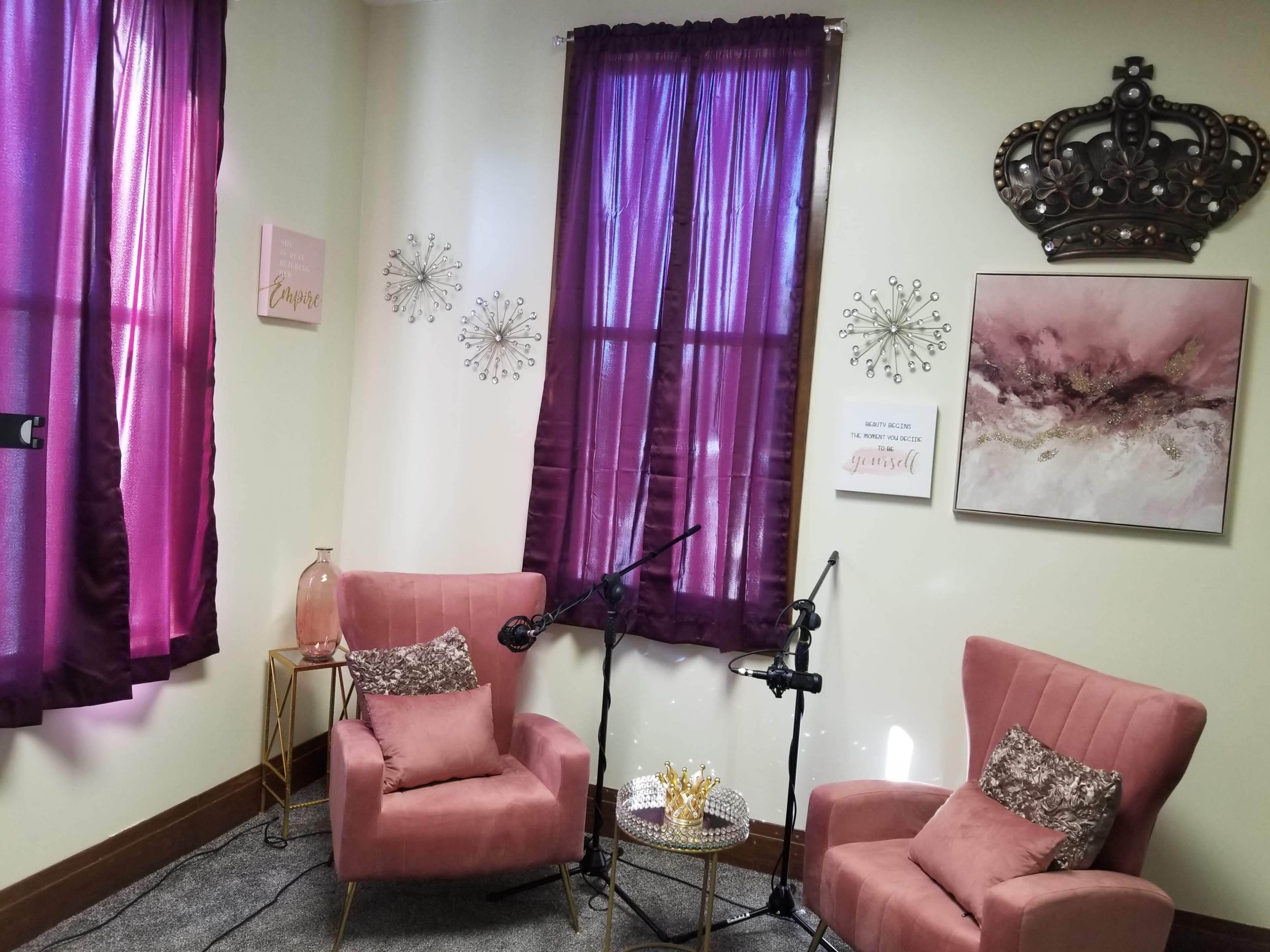 A small, elegantly decorated room with two pink armchairs, purple curtains, and artwork on the walls.