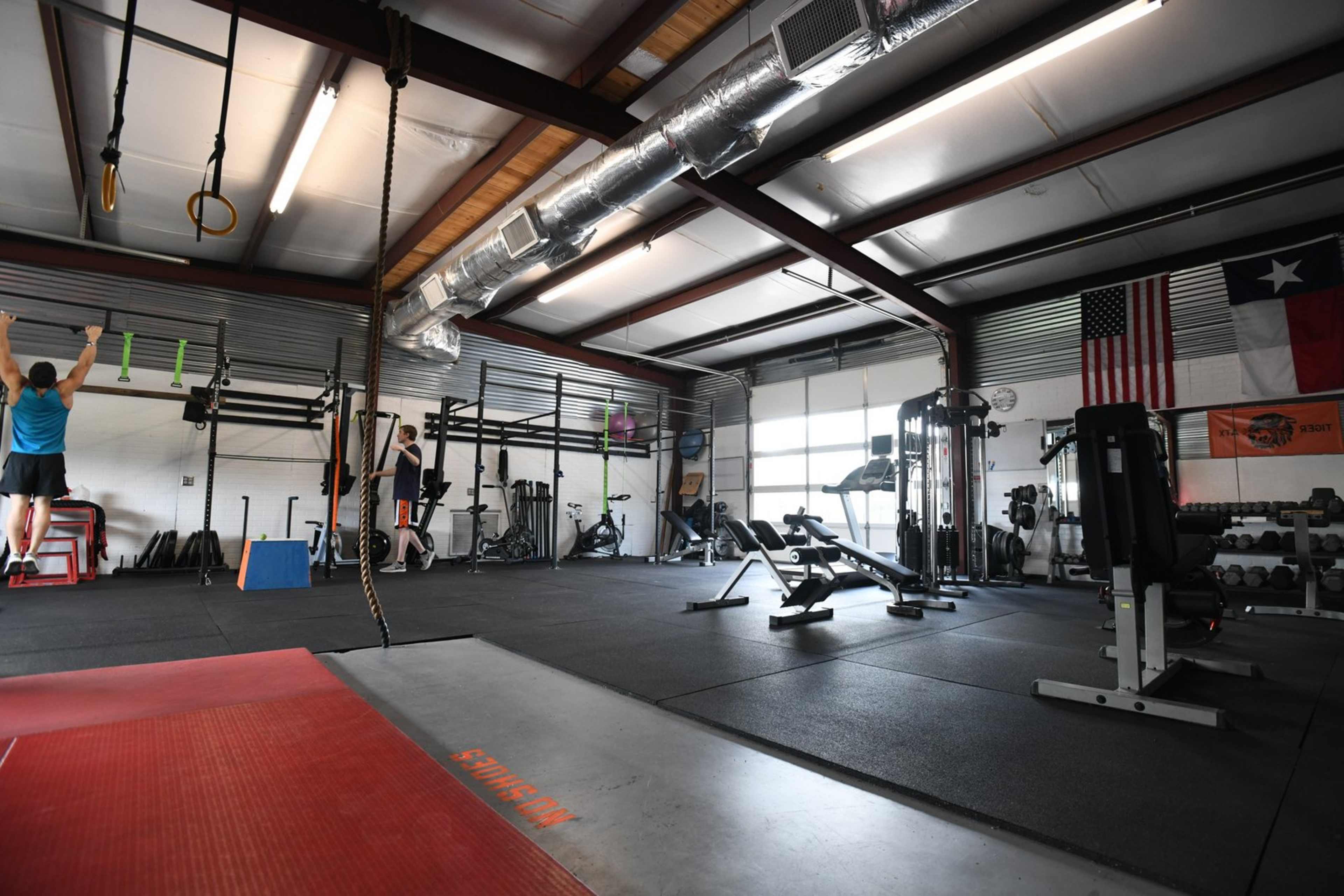 A gym interior with exercise equipment, including weights and benches, and individuals performing workouts in a spacious, well-lit area.