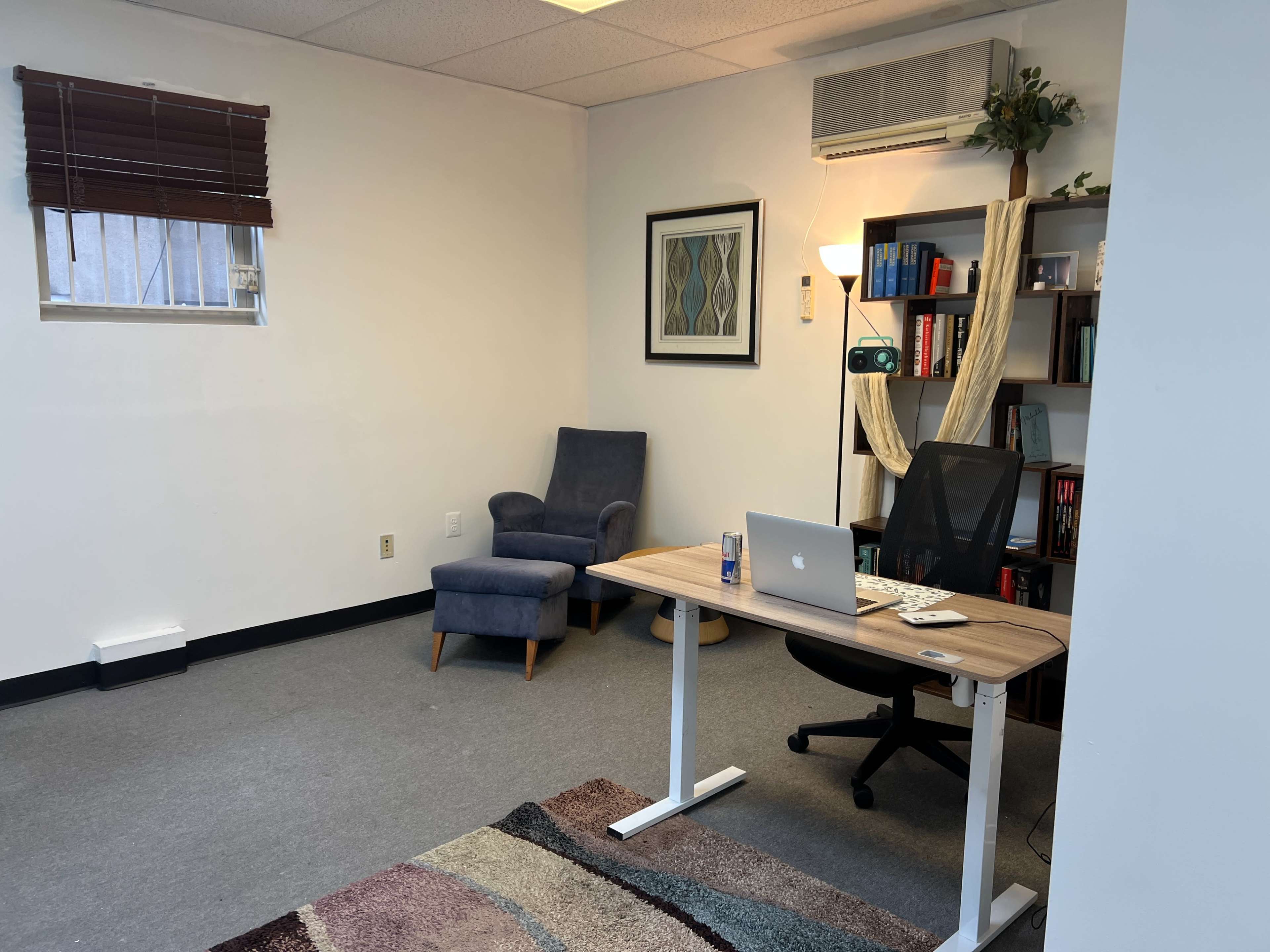 The image shows a minimalistic office space with a desk, a chair, and a bookshelf against a white wall.