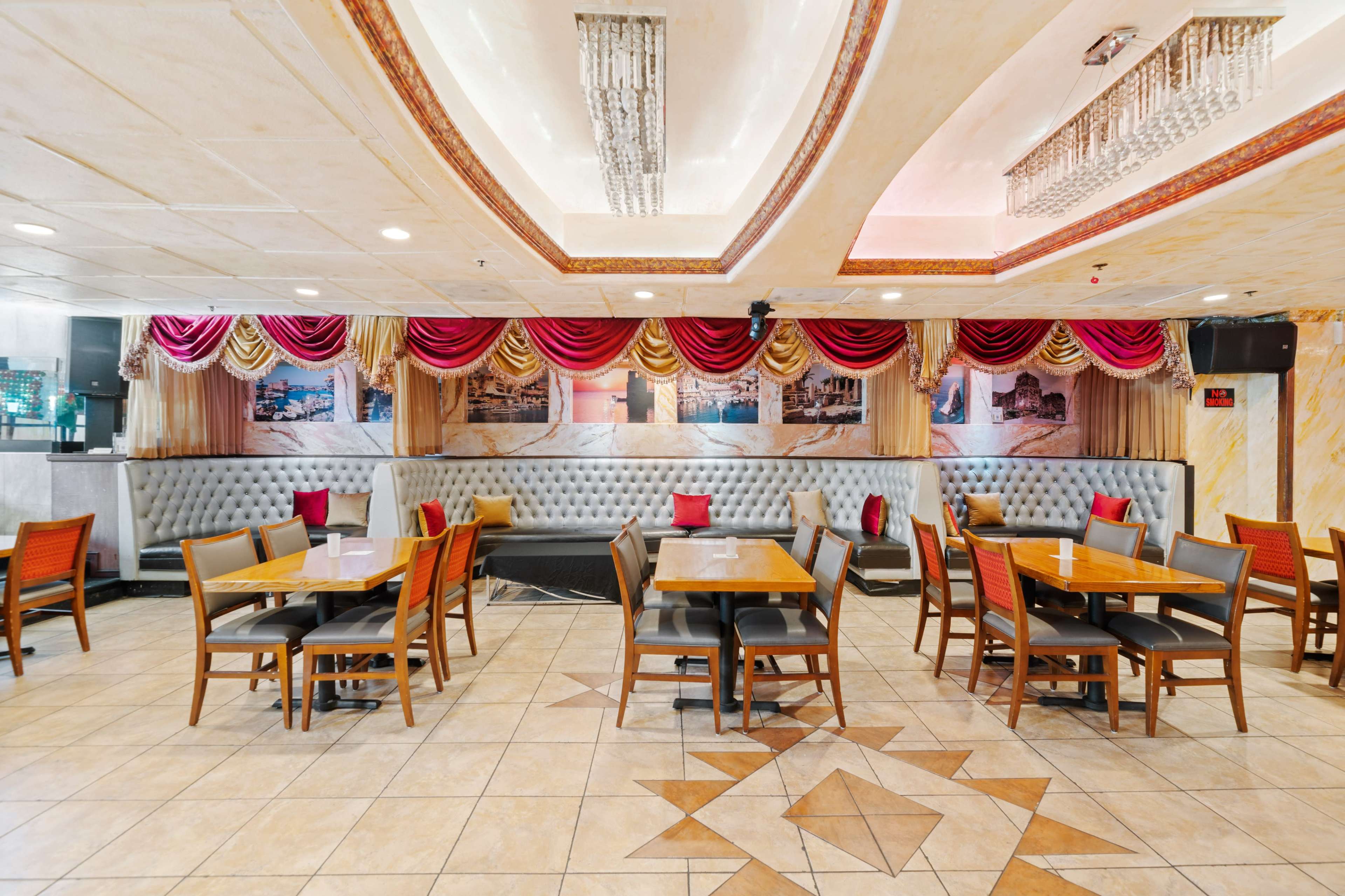 A neatly arranged restaurant interior featuring tables and chairs, decorative red and gold curtains, and a patterned floor tile.