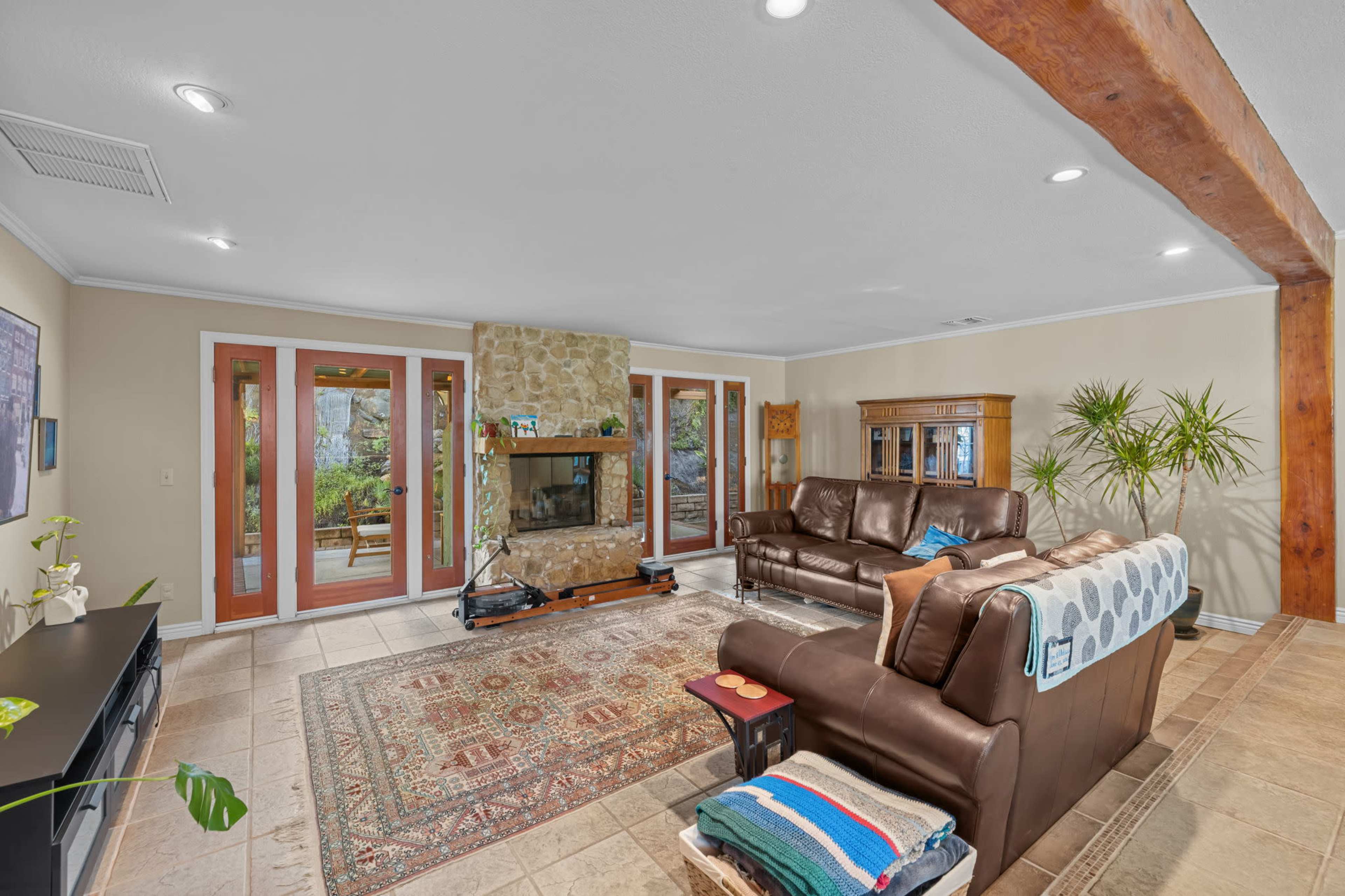The living room features a stone fireplace, leather sofas, and large windows overlooking a patio.