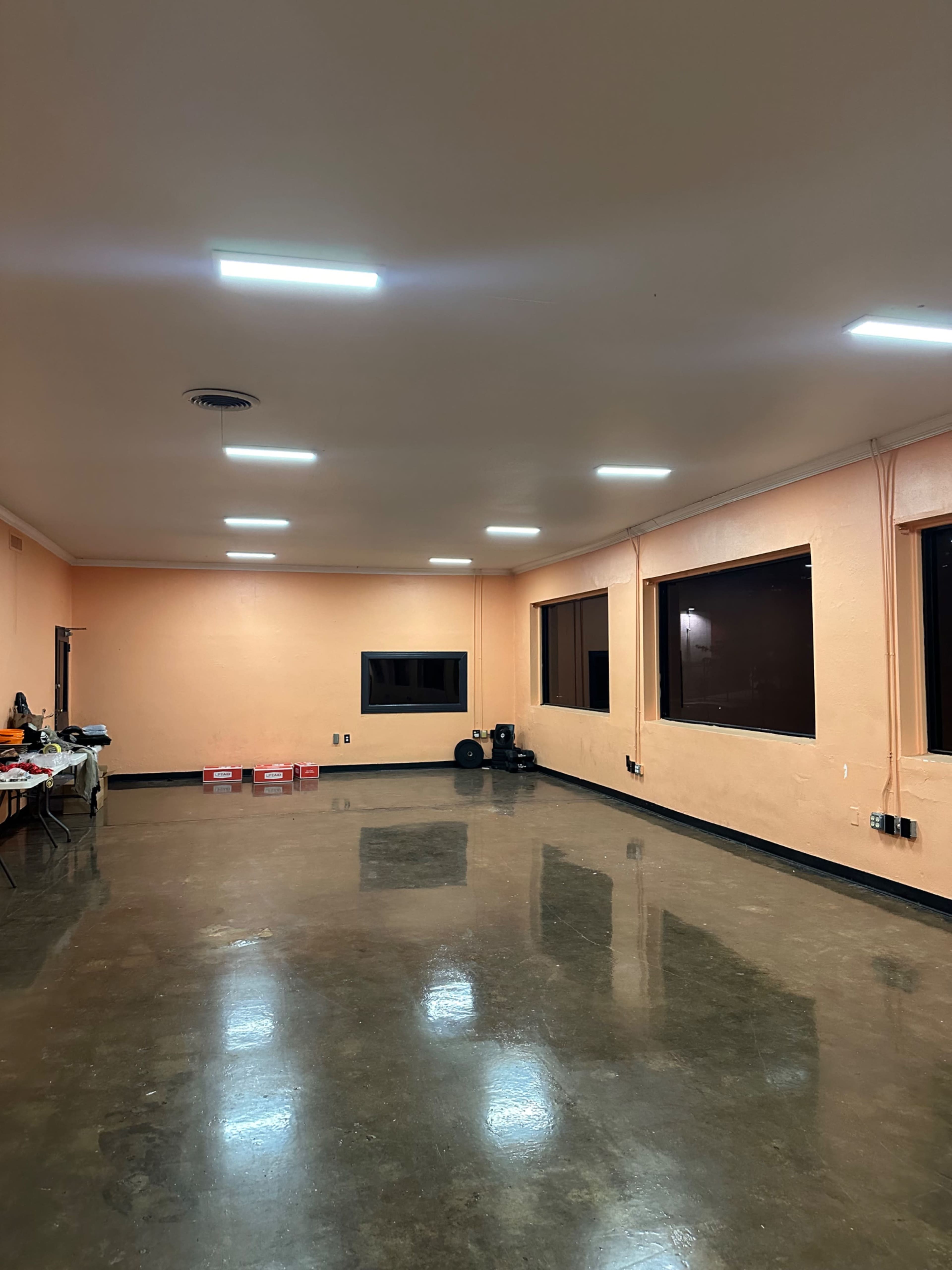 The image shows an empty room with orange walls, a polished concrete floor, and fluorescent lighting on the ceiling.