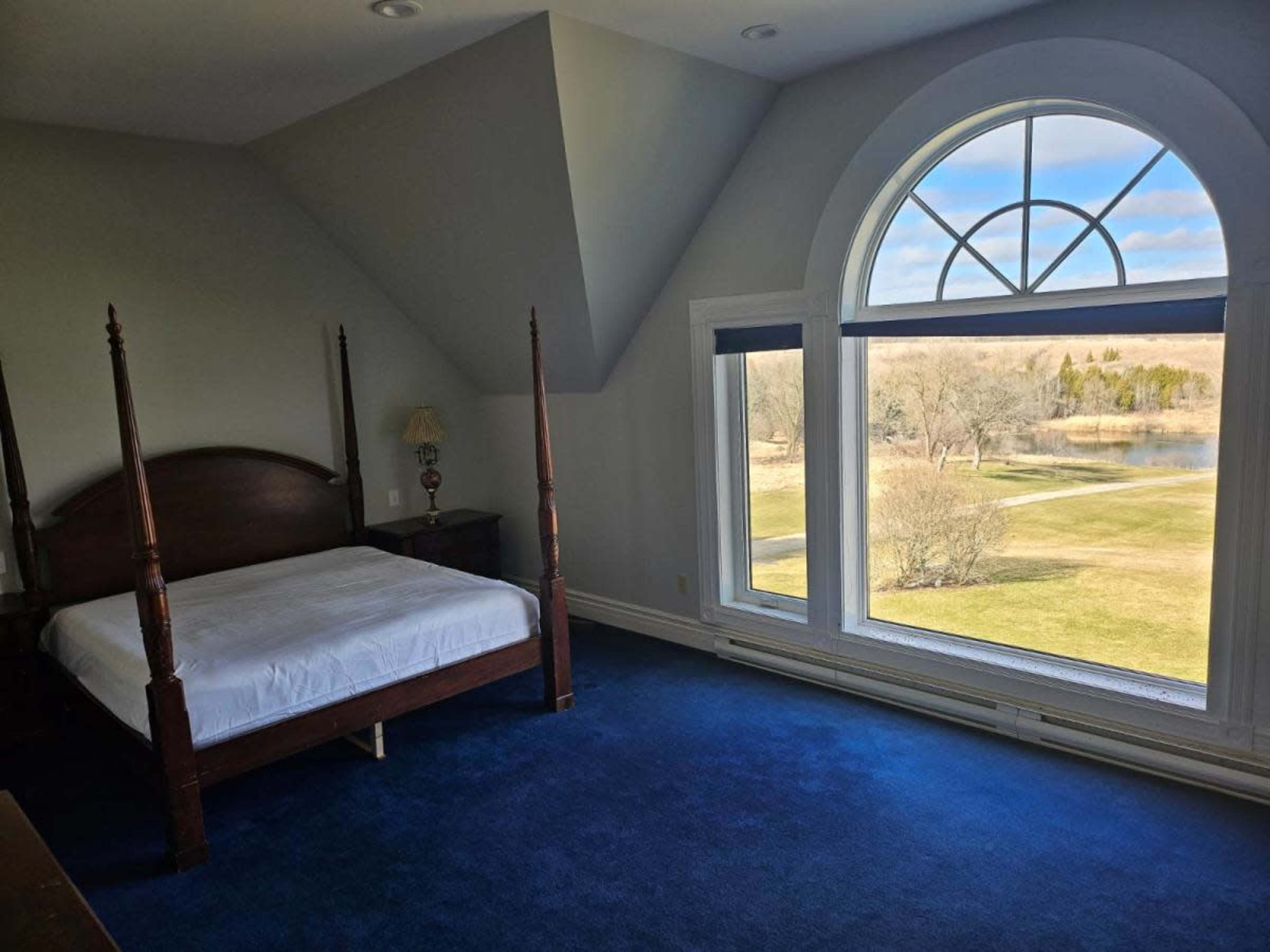 A spacious bedroom with a four-poster bed, large windows, and views of a landscape outside.
