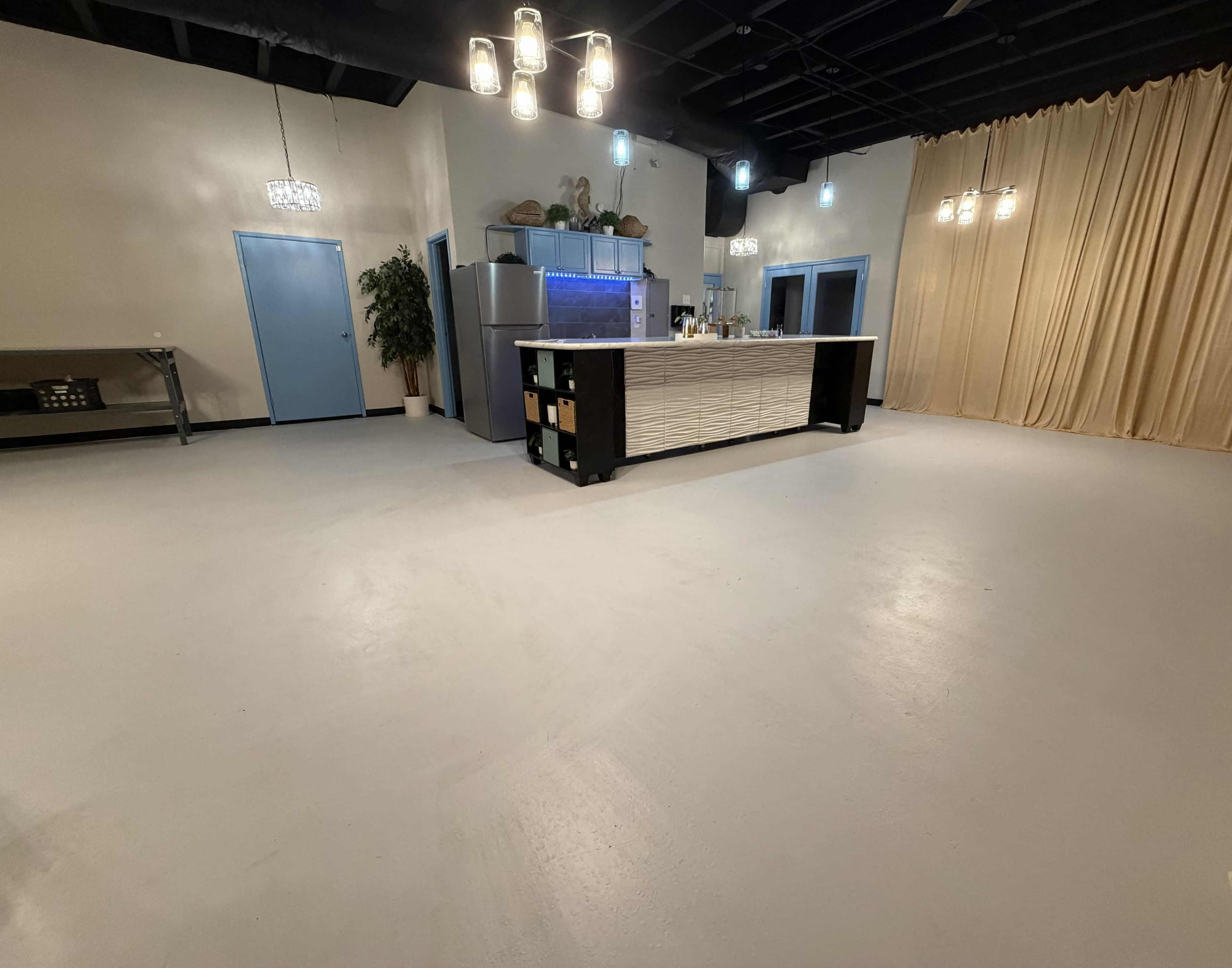 The image shows a spacious interior with a bar counter, a large cream-colored curtain, and blue doors in a well-lit environment.