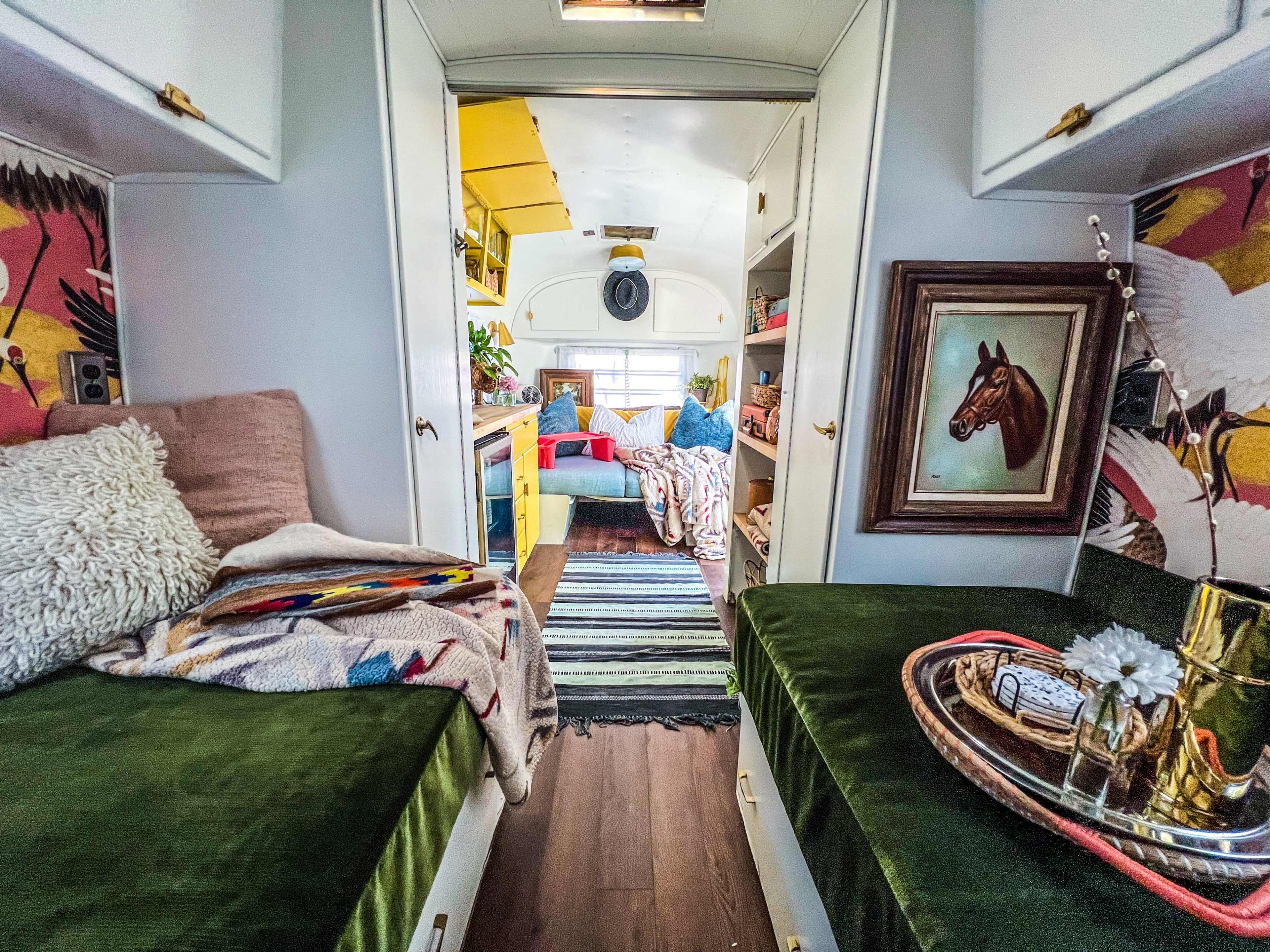 A colorful, renovated vintage trailer interior featuring seating areas with green cushions, floral wallpaper, and various decorative items.