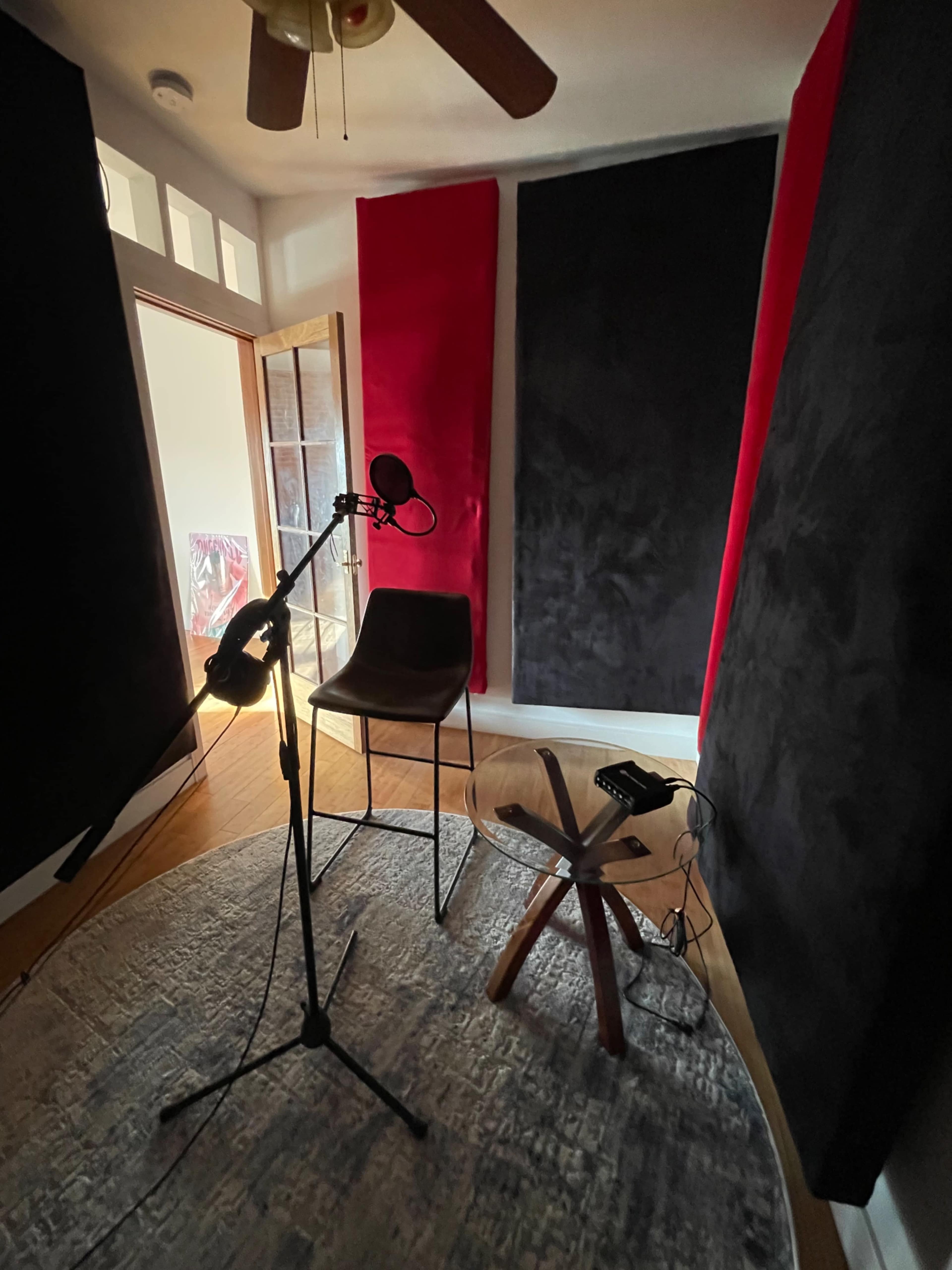 A recording studio setup with a microphone on a stand, a chair, and soundproofing panels in black and red.