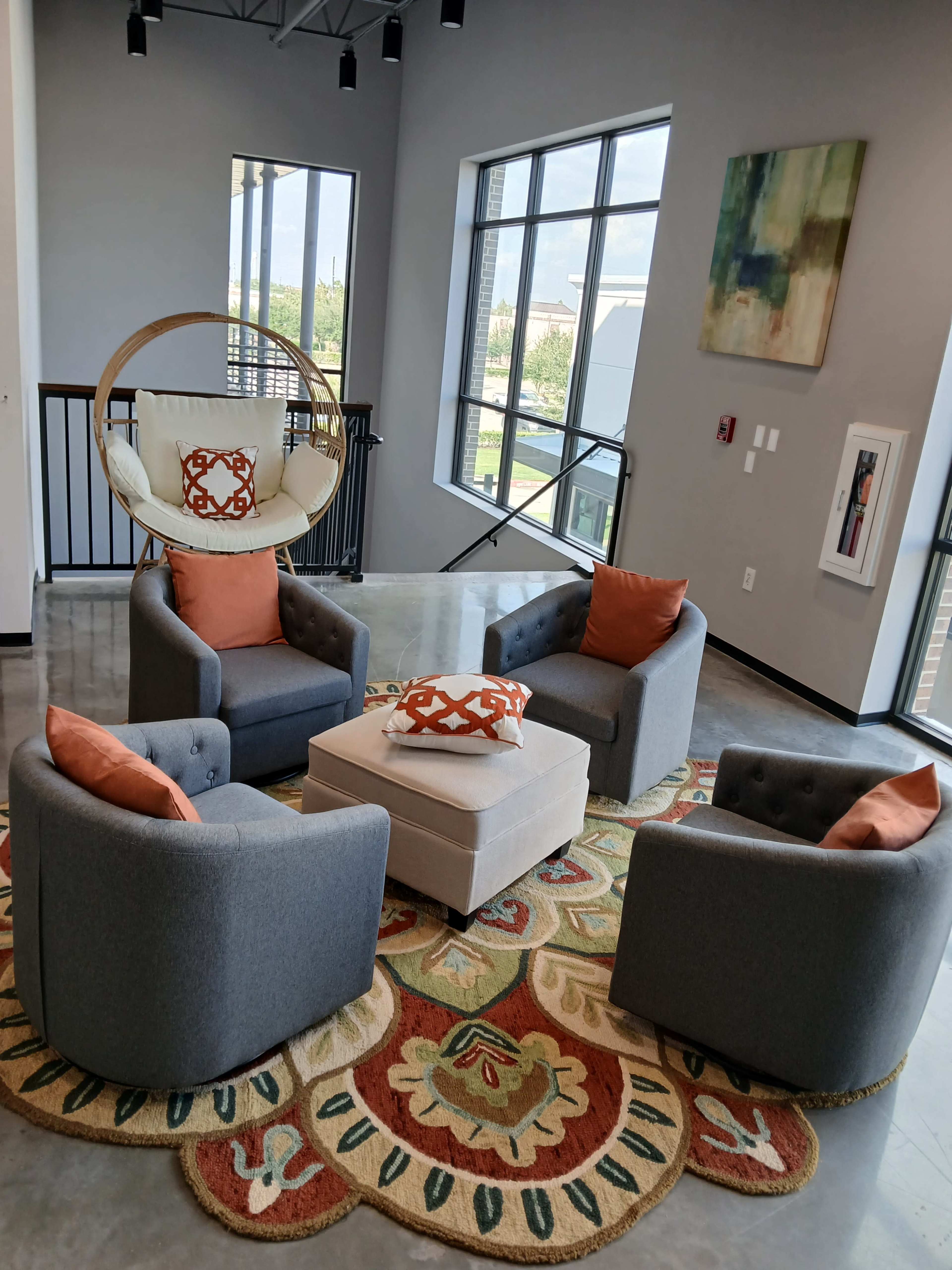 The image depicts a seating area with four gray armchairs and an oval hanging chair arranged around a central white coffee table on a patterned rug.