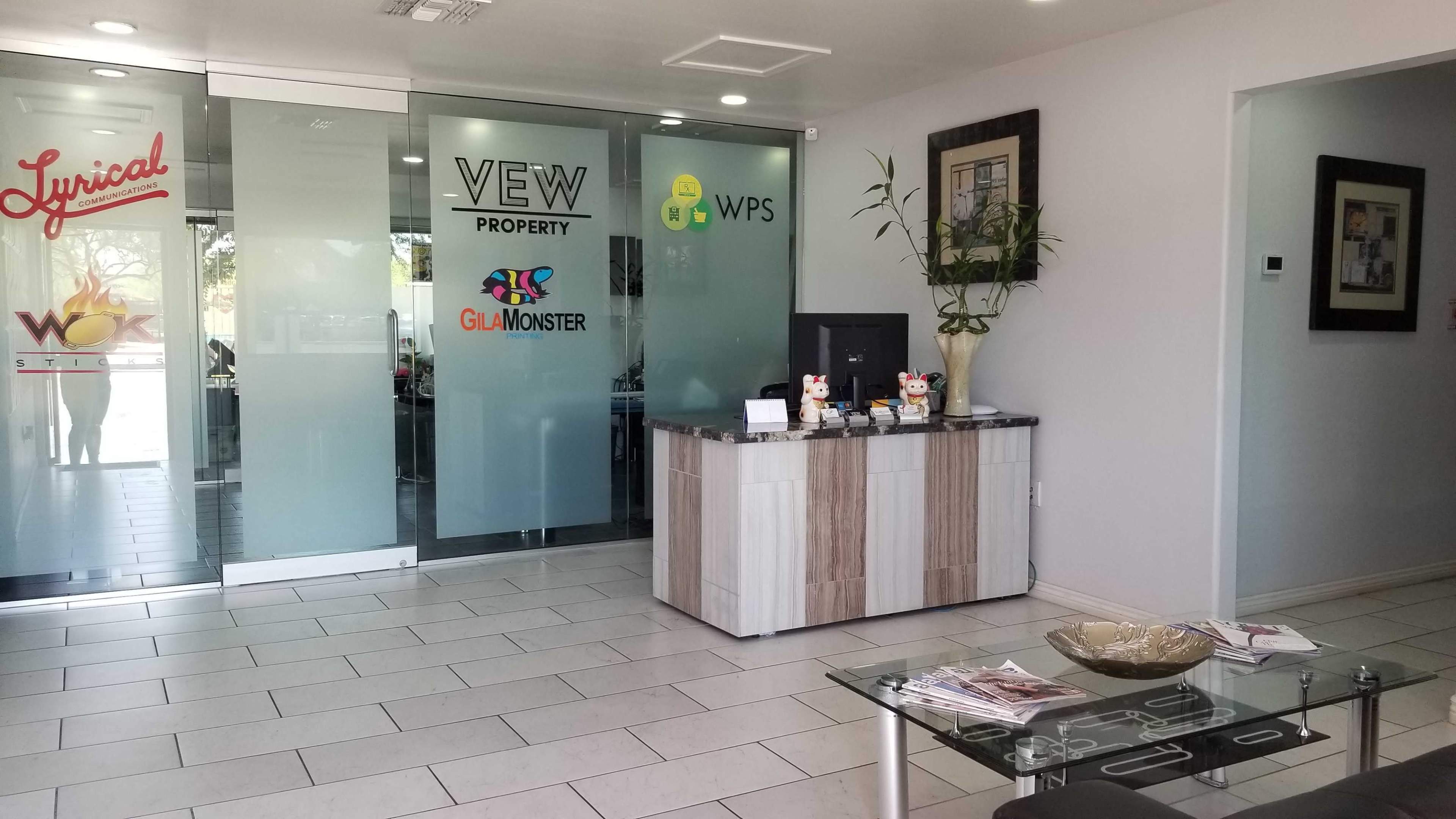 A modern office reception area with a glass wall featuring various logos and a sleek desk with decorations and informational materials.