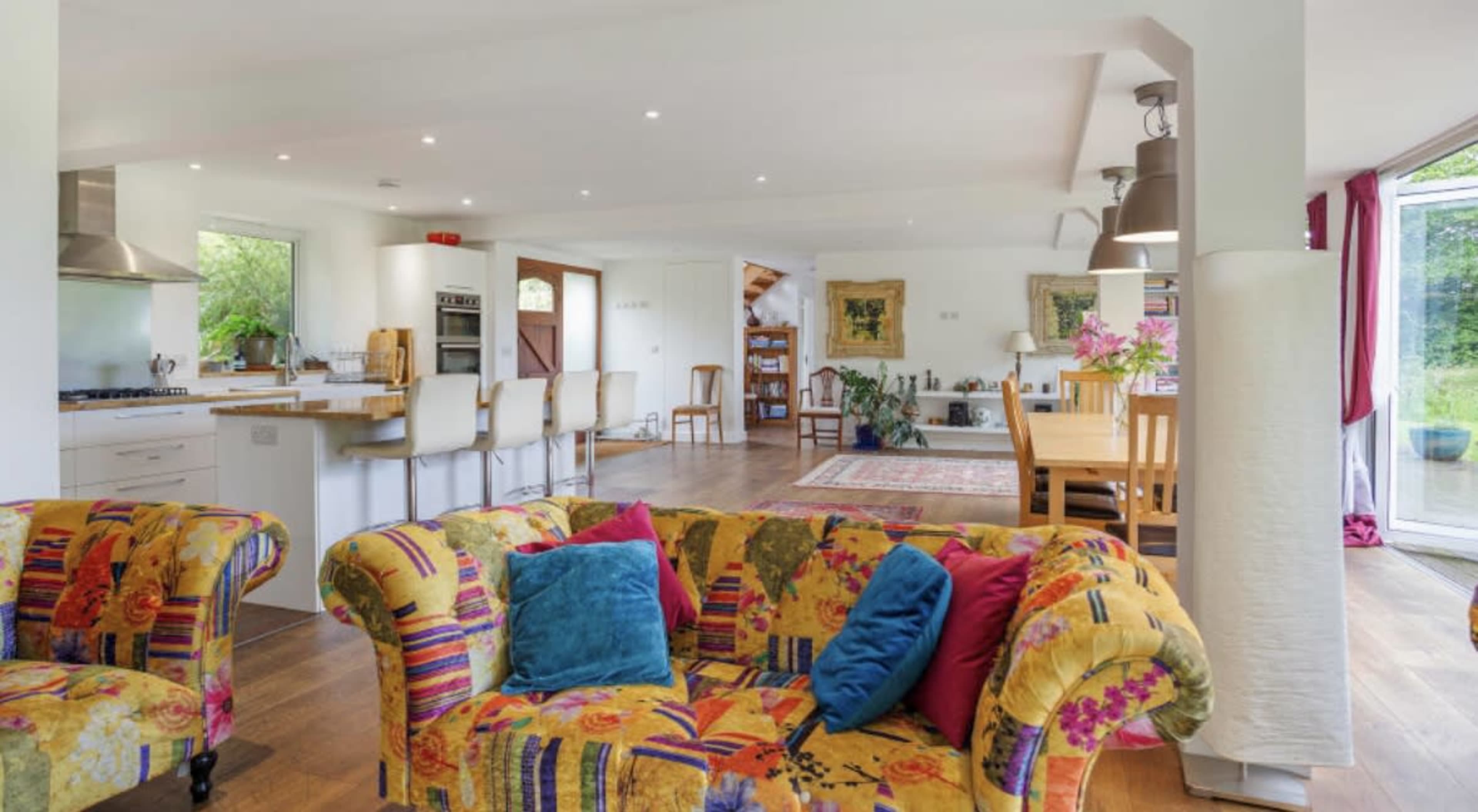 A spacious open-plan living and dining area with colorful furniture, modern appliances, and natural light flowing through large windows.